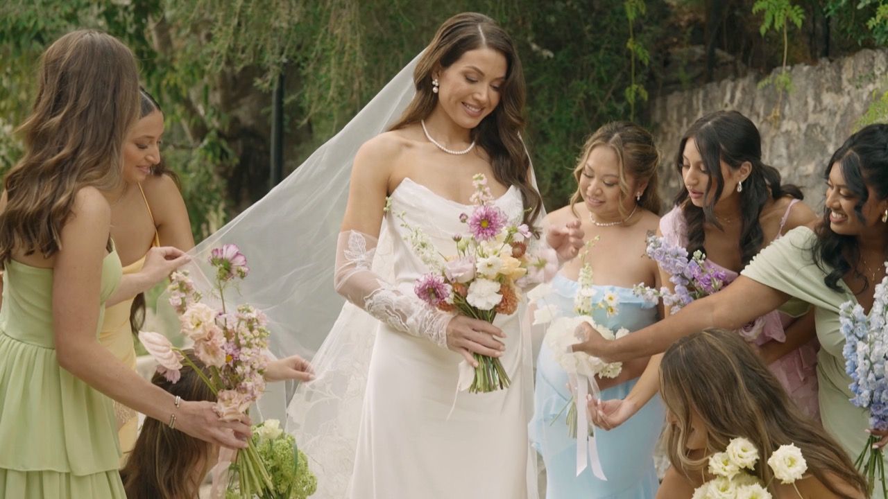 Bride surrounded by her bridesmaids, all smiling and adjusting the details of her dress and bouquet.