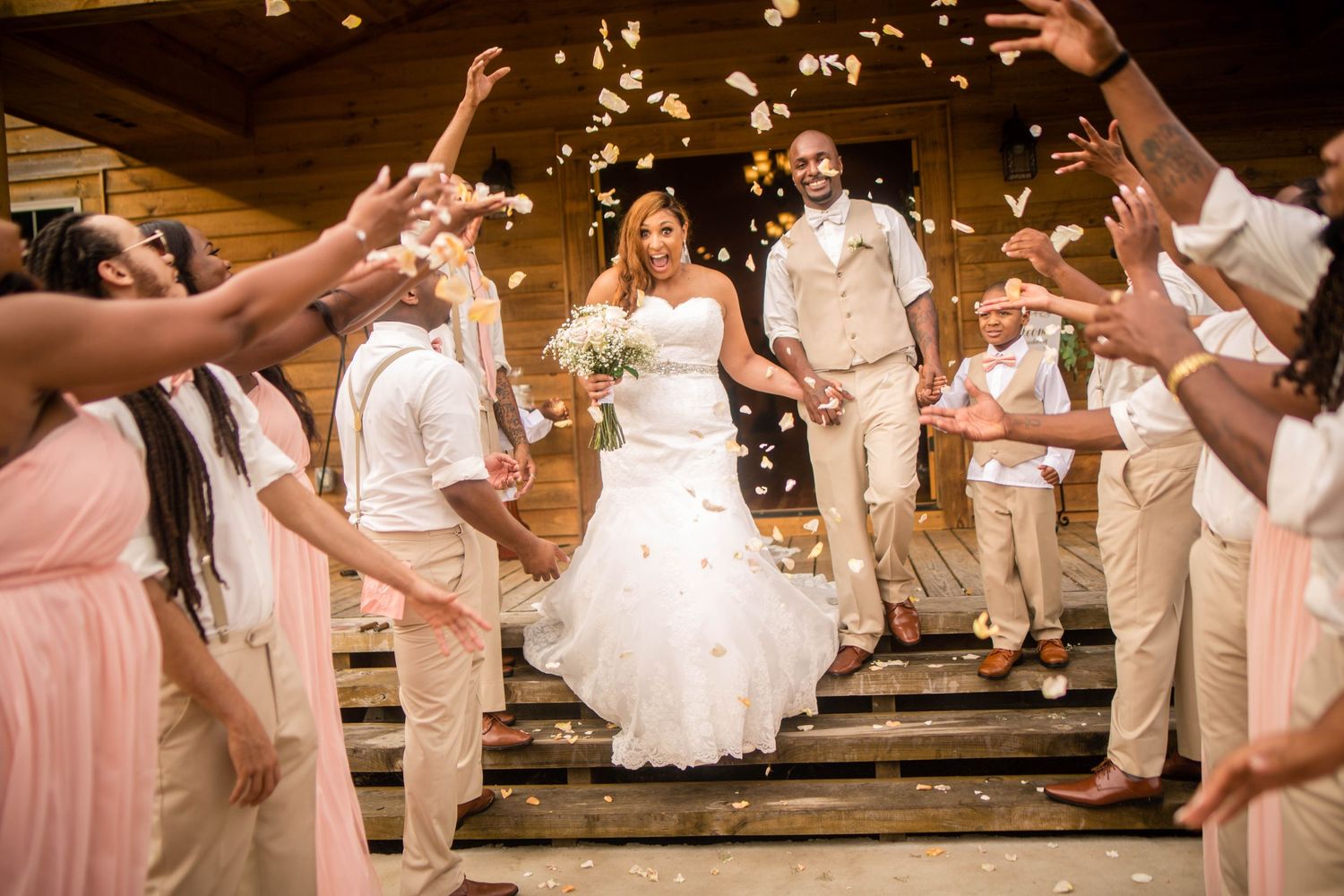 Wedding celebration with bridal party in white and pink dresses dancing on wooden floor.