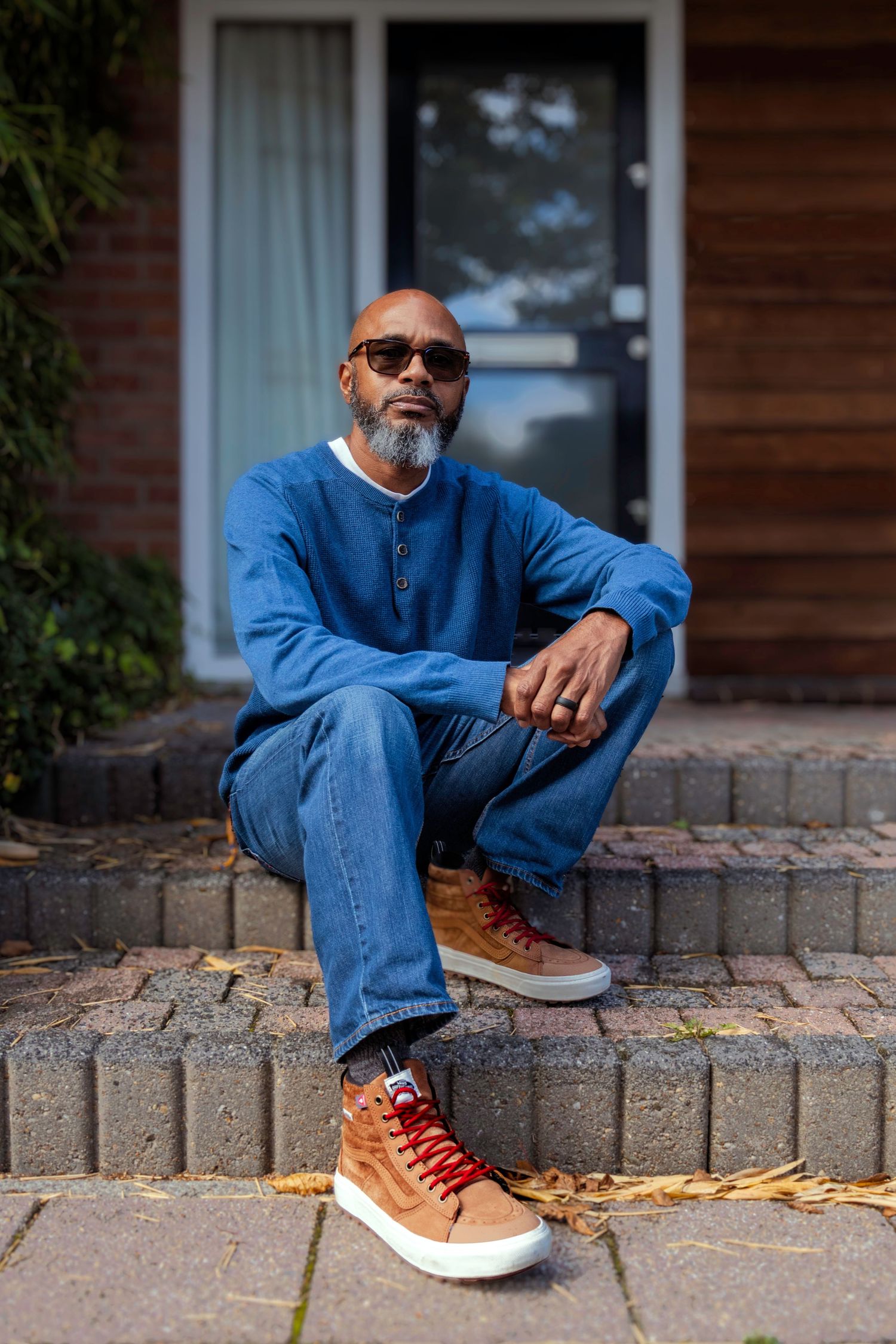 Person in a blue shirt and jeans sits casually on brick steps wearing brown leather boots and sunglasses.
