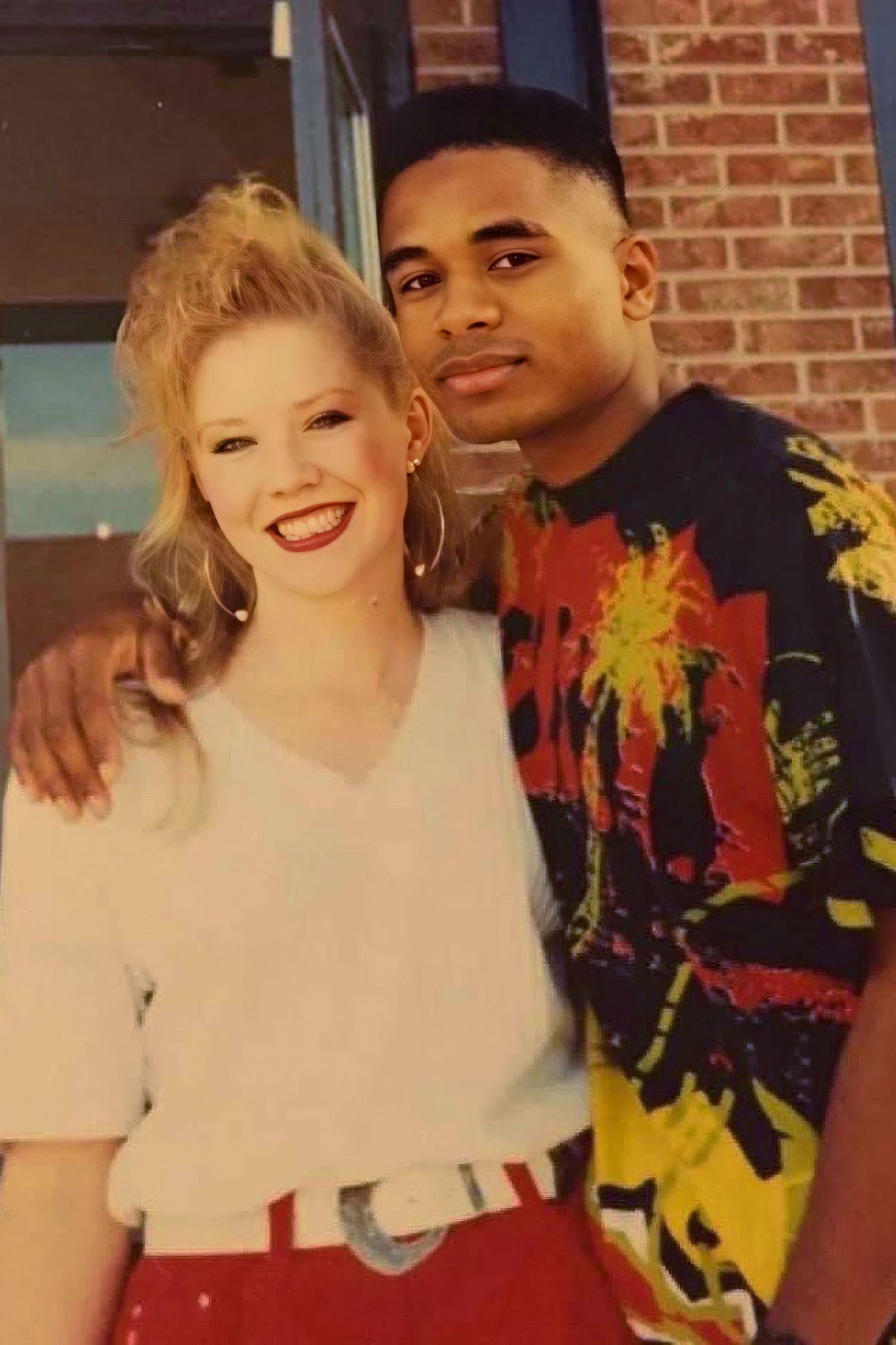 A vintage 90s photo showing a couple in bright clothing against a brick wall background.