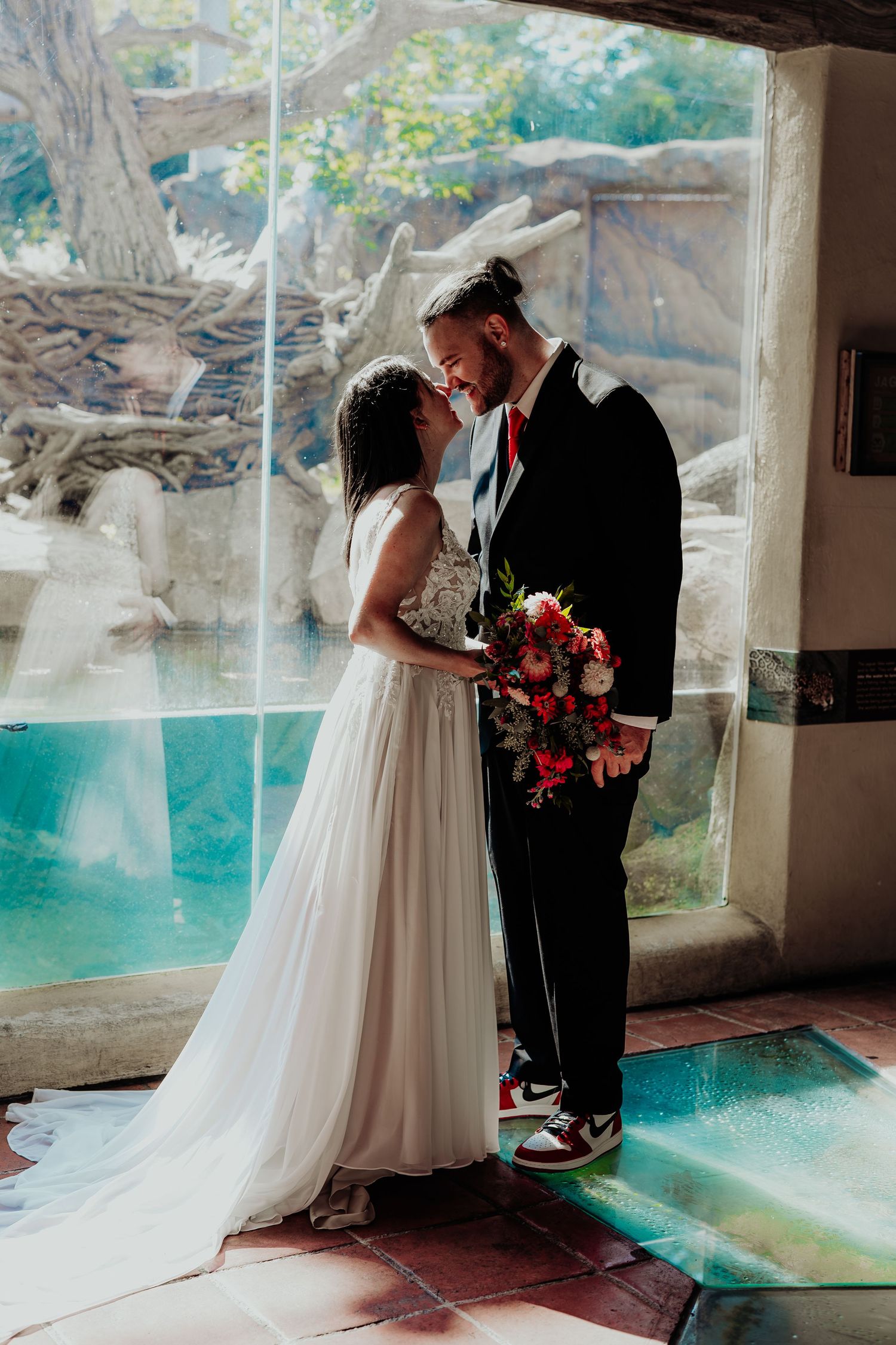 A wedding couple stands in front of an aquarium tank with turquoise water creating a romantic underwater backdrop.