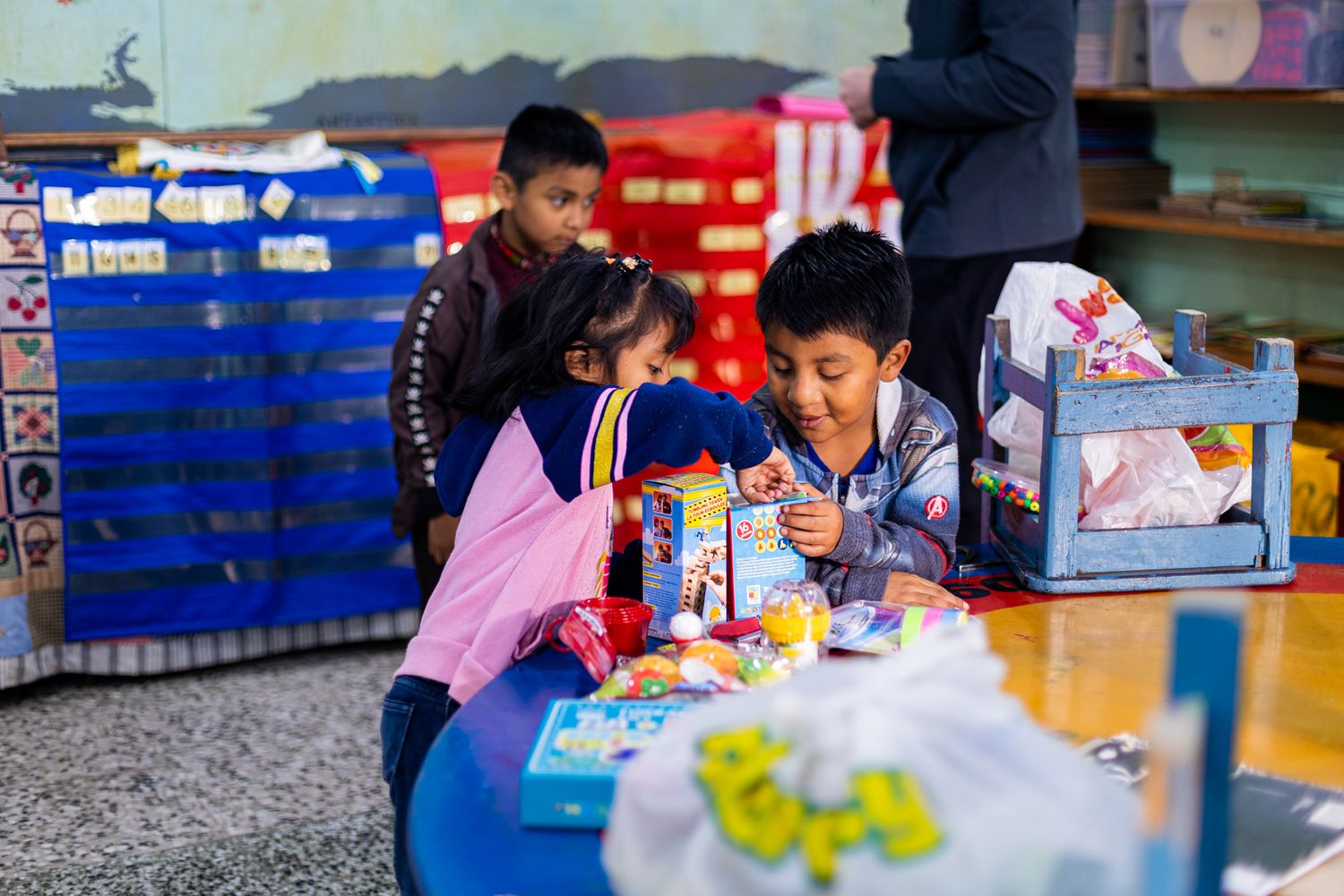 Children gathered around a blue table engaged in an activity with colorful supplies.