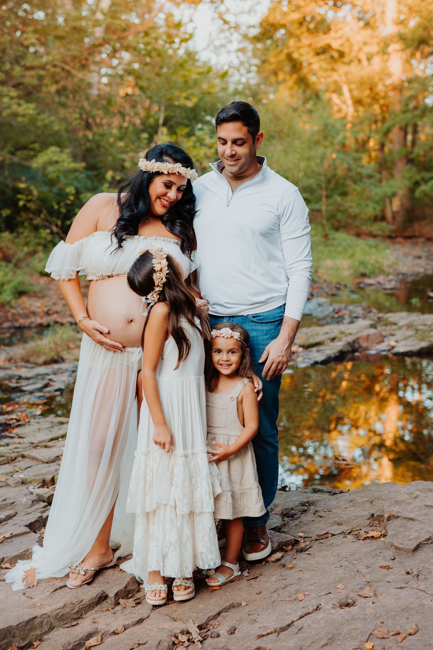 Family enjoying a warm autumn day together by a creek with golden foliage reflecting in the water.