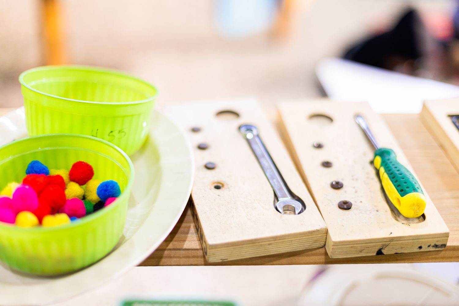 Educational wooden board with colorful manipulatives and a green bowl of supplies.