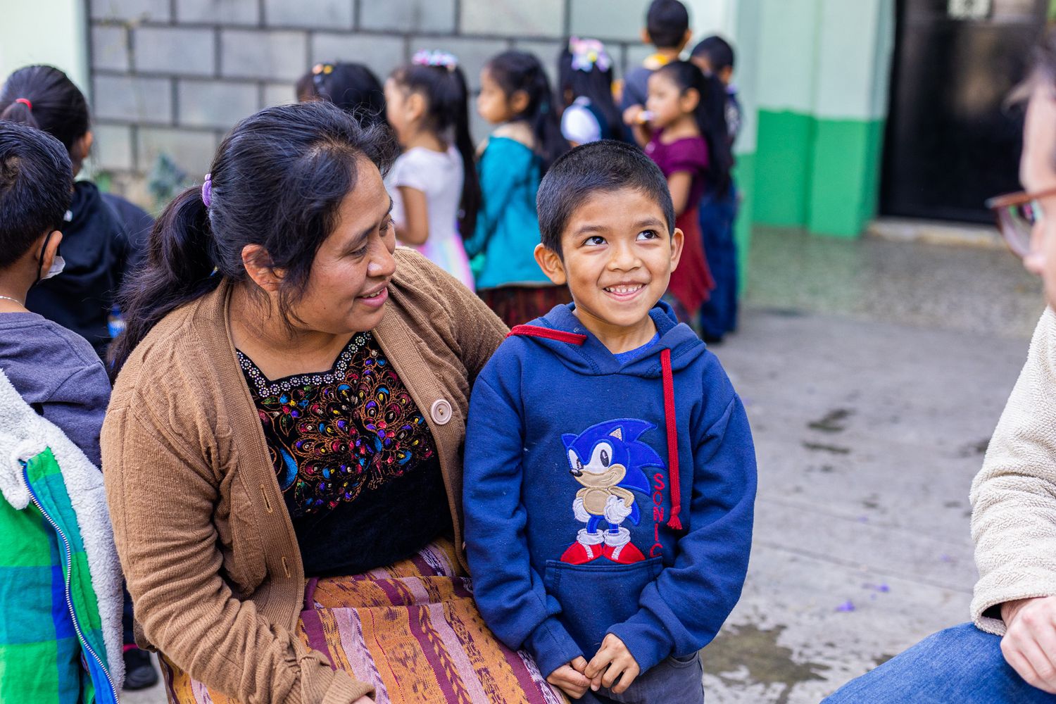 Students and adults gather outside a school building with bright green painted walls.