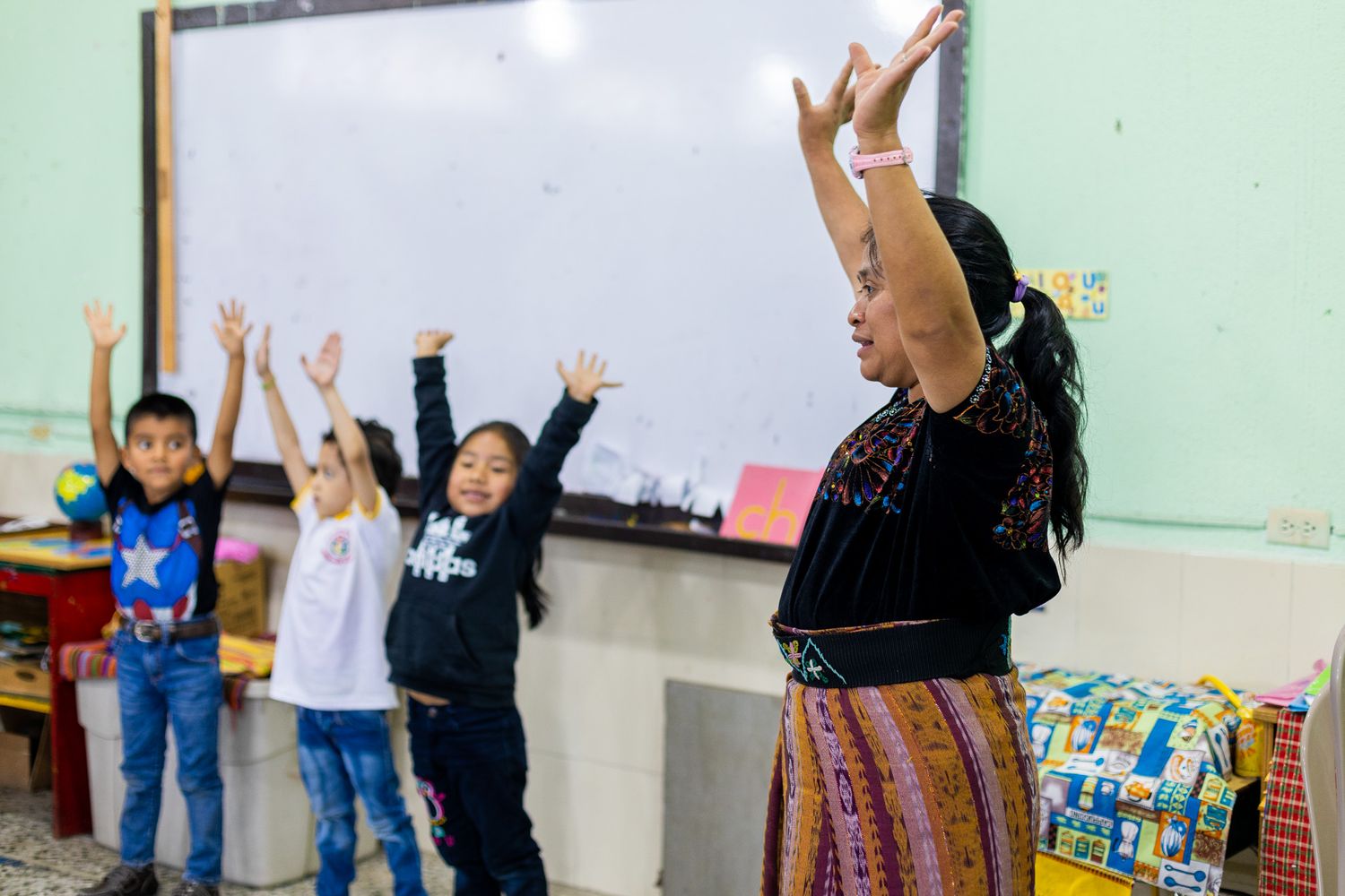 Students and teachers participate in an energetic classroom activity with raised arms.