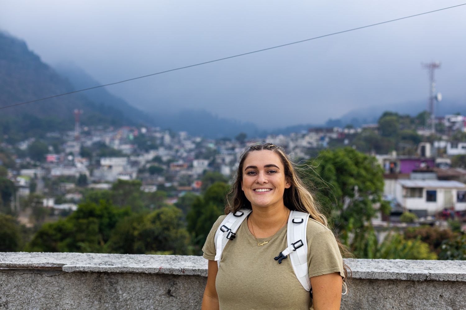Traveler smiling with a backpack against a misty mountain town backdrop.