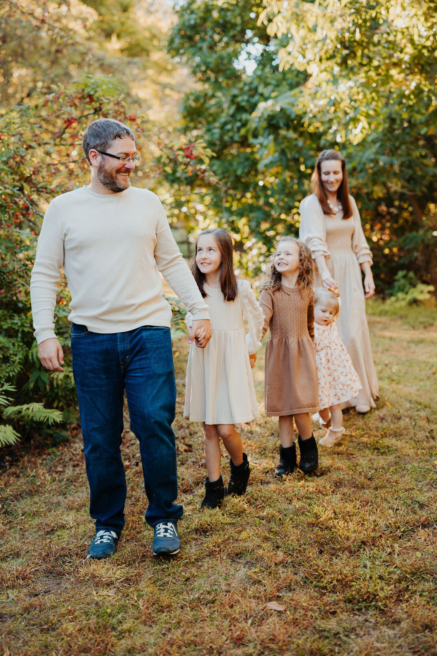 Family group wearing coordinated brown and beige outfits walks together in a sunlit autumn garden setting.