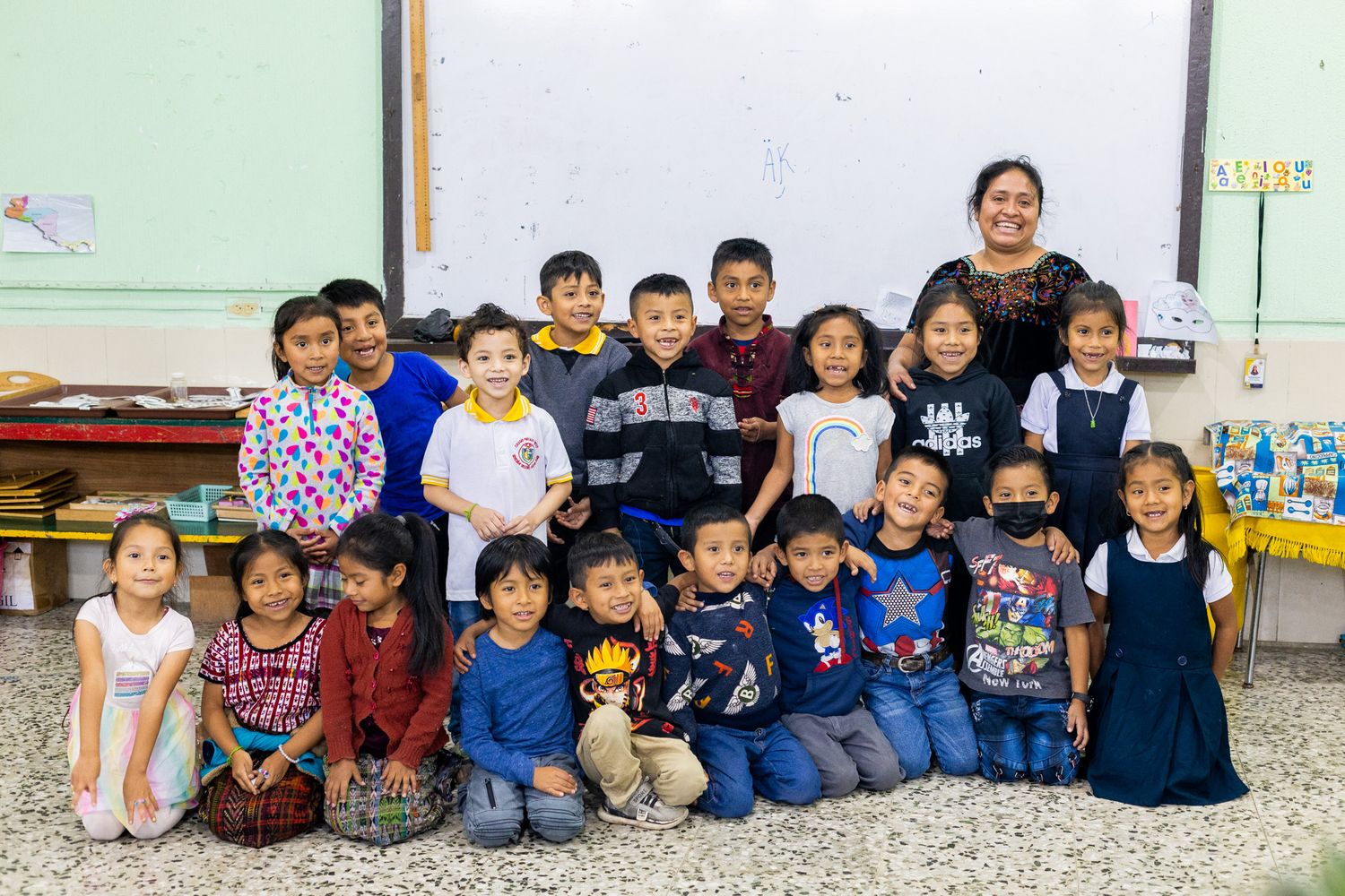 Large group photo of students and teacher in a bright classroom setting.