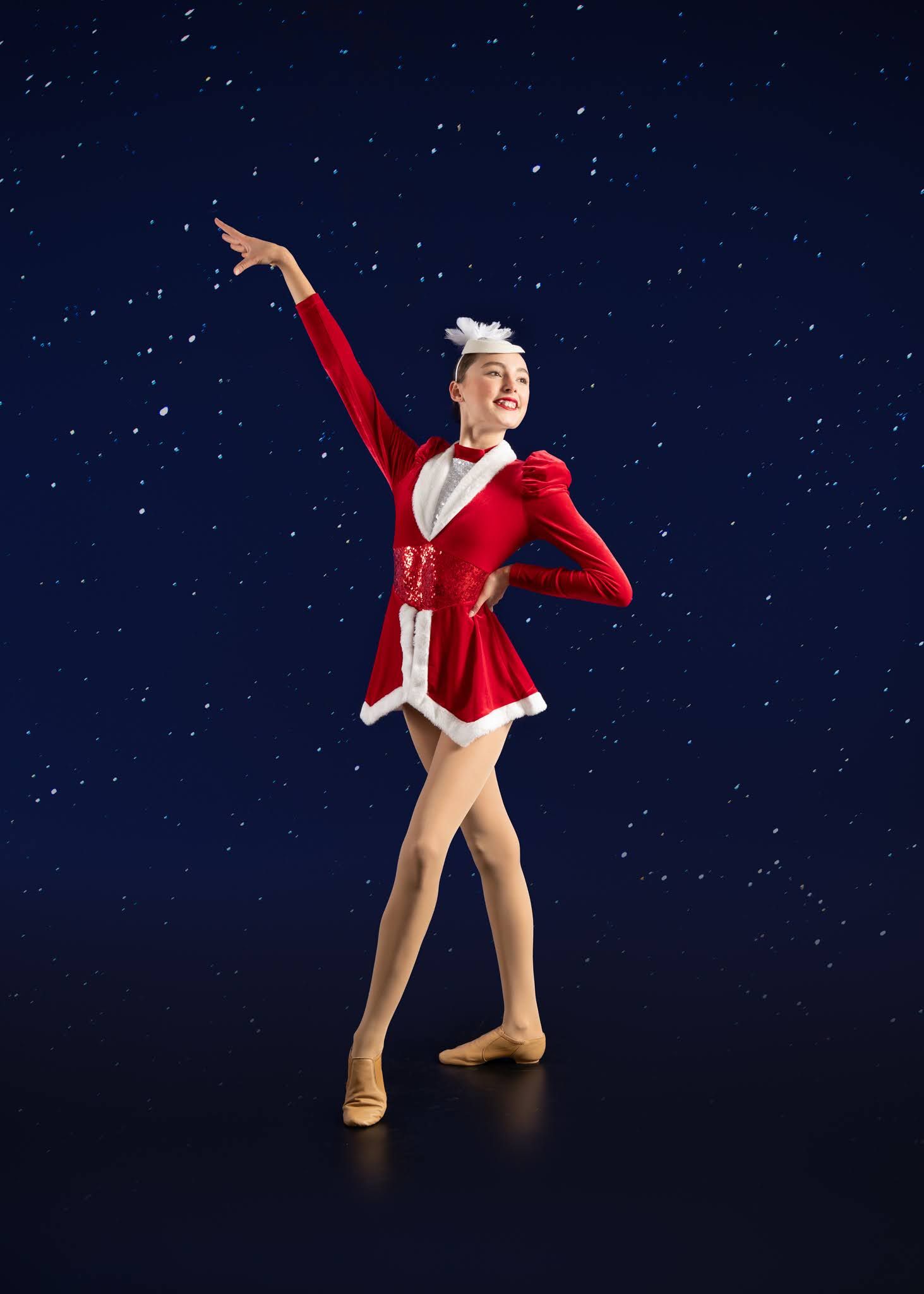 Smiling dancer in red Santa costume performs festive holiday ballet routine against snowy night sky.