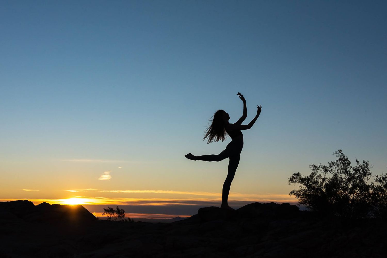Silhouette of a dancer striking a graceful pose against a vibrant sunset sky outdoors.