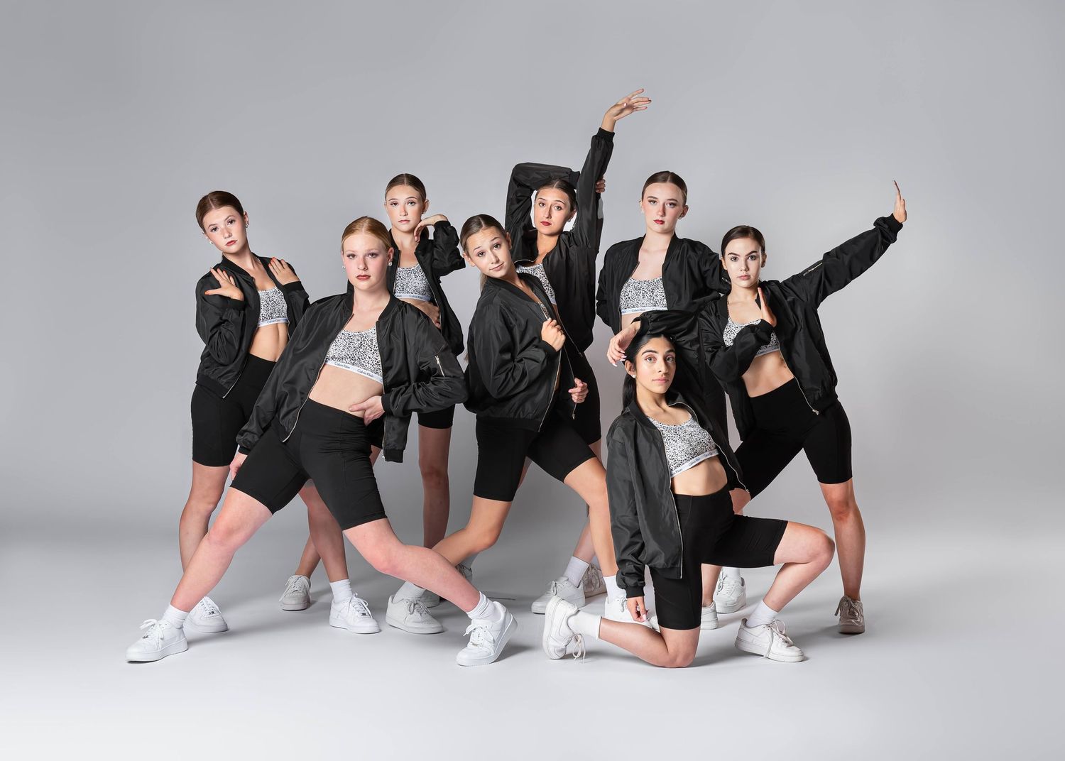 Dance team of ten performers strike dynamic poses in black jackets and shorts.