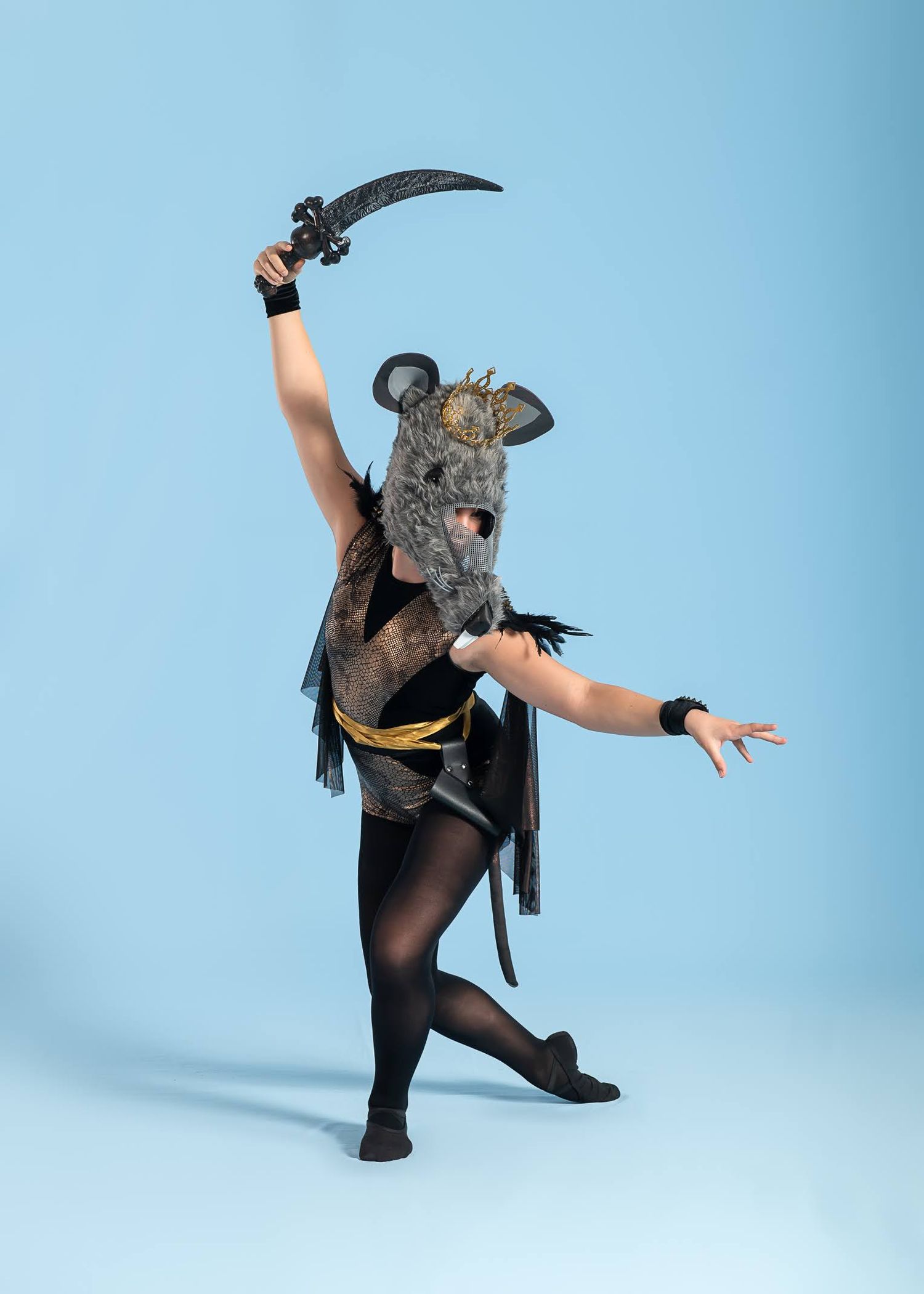 Dancer in rat costume with mask and sword performs ballet on a light blue studio background.