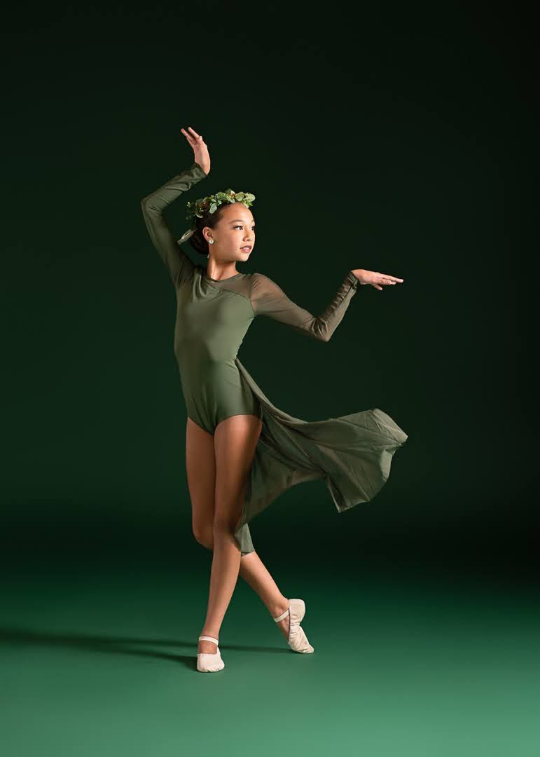 Ballet dancer in olive green leotard and floral crown performs contemporary dance on green backdrop.