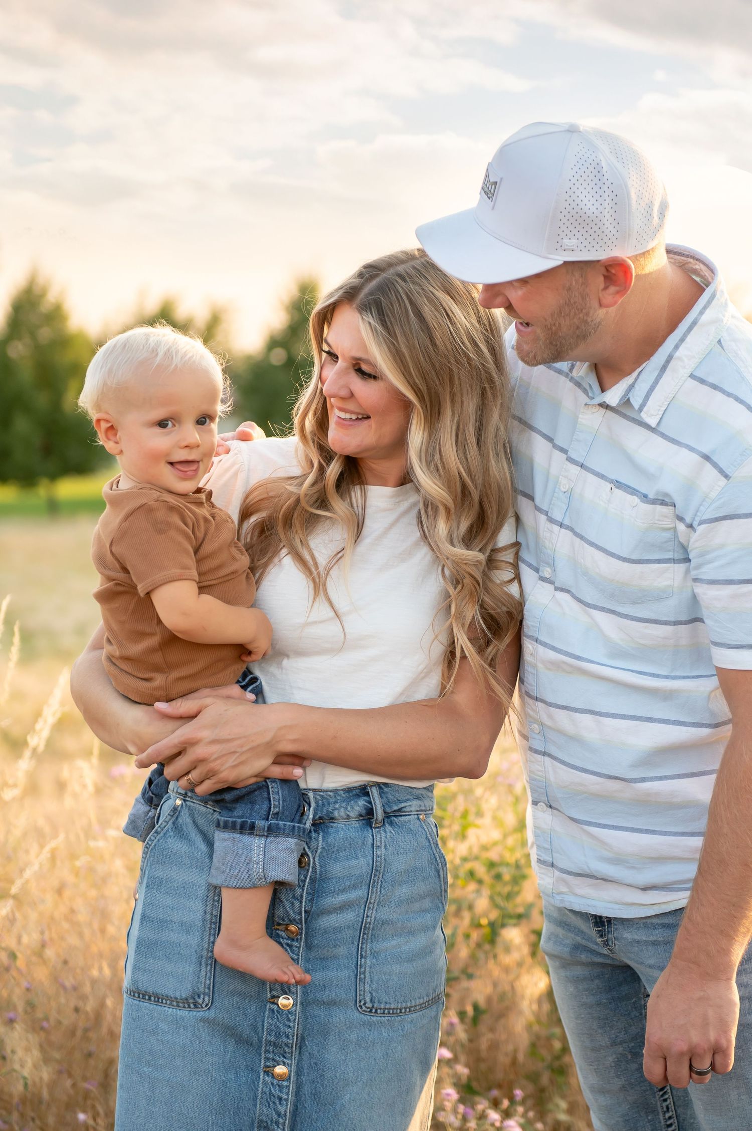 Young family with a toddler smiling together in a sunlit meadow.
