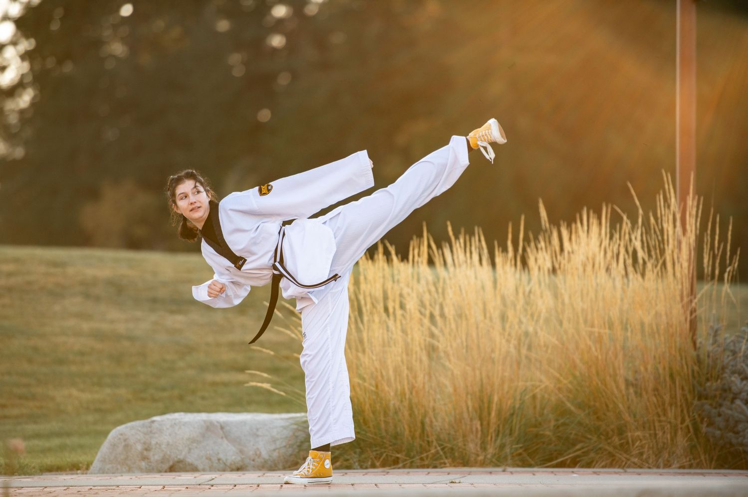 Martial artist in white uniform performing high kick outdoors in golden sunlight.