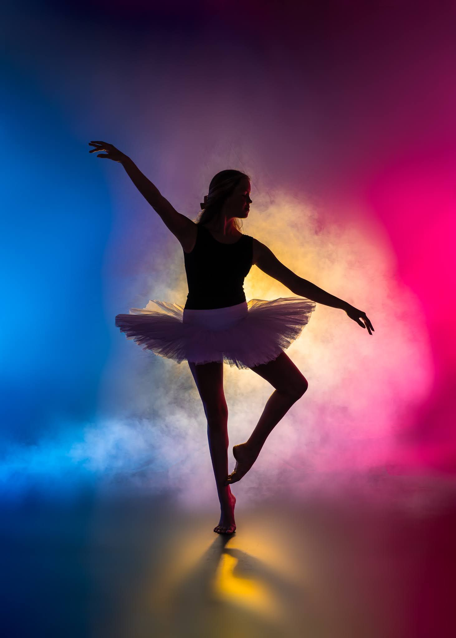 Silhouette ballerina in white tutu dancing in colorful neon smoke backdrop.