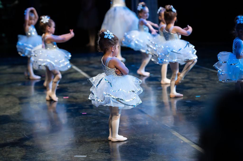 Young ballerinas in white tutus performing on stage during a childrens ballet recital.