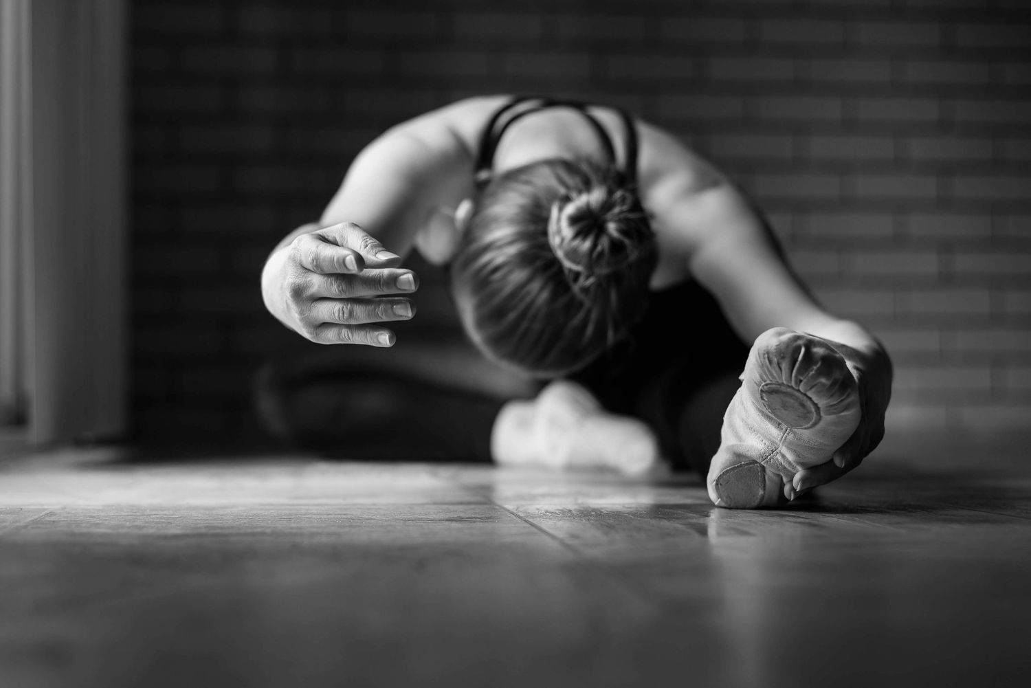 Ballet dancer stretches forward in deep floor pose wearing ballet slippers in black and white.