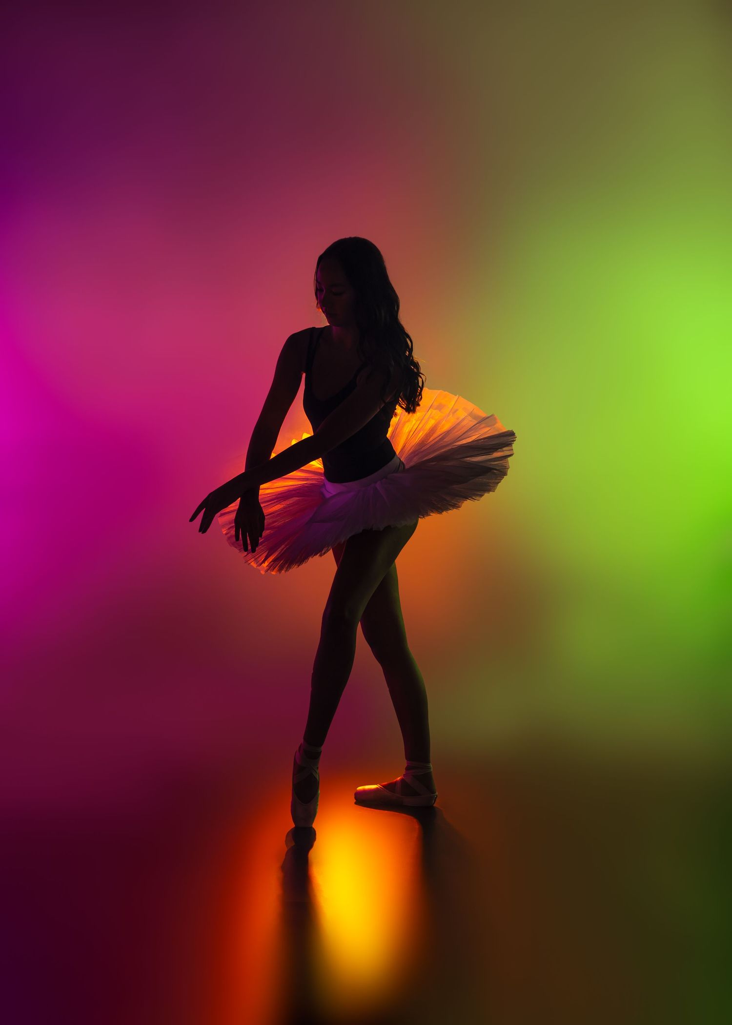Silhouette ballerina in tutu on pointe in pink green neon gradient lighting.