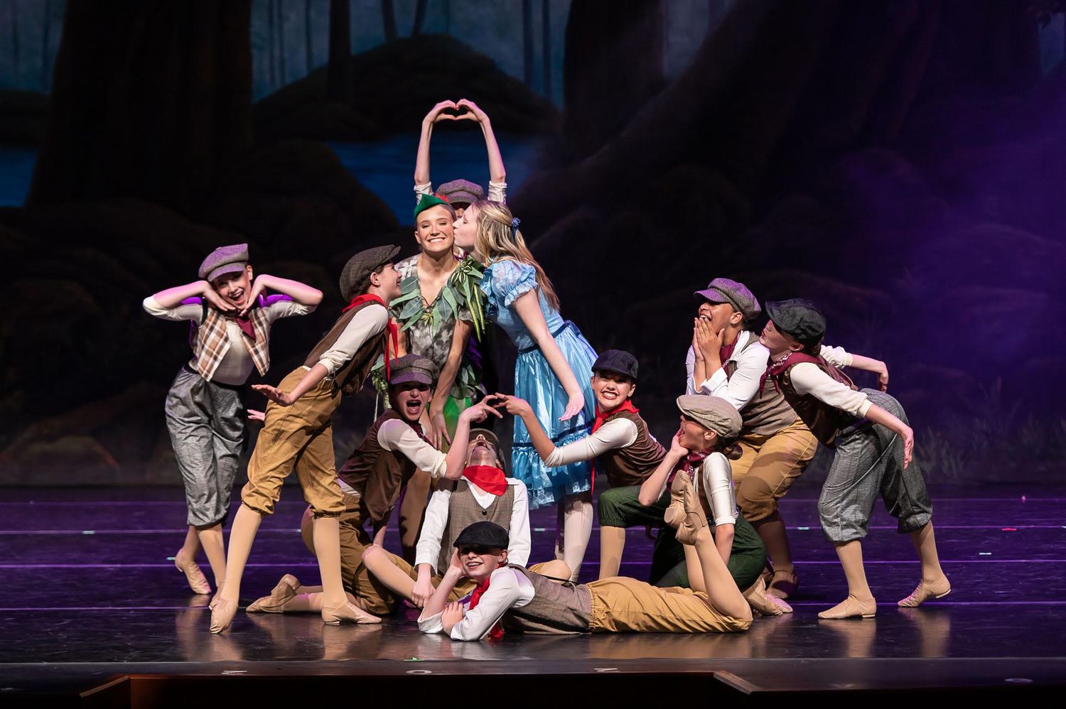 Peter Pan ballet performance with costumed dancers grouped together on stage with forest backdrop.