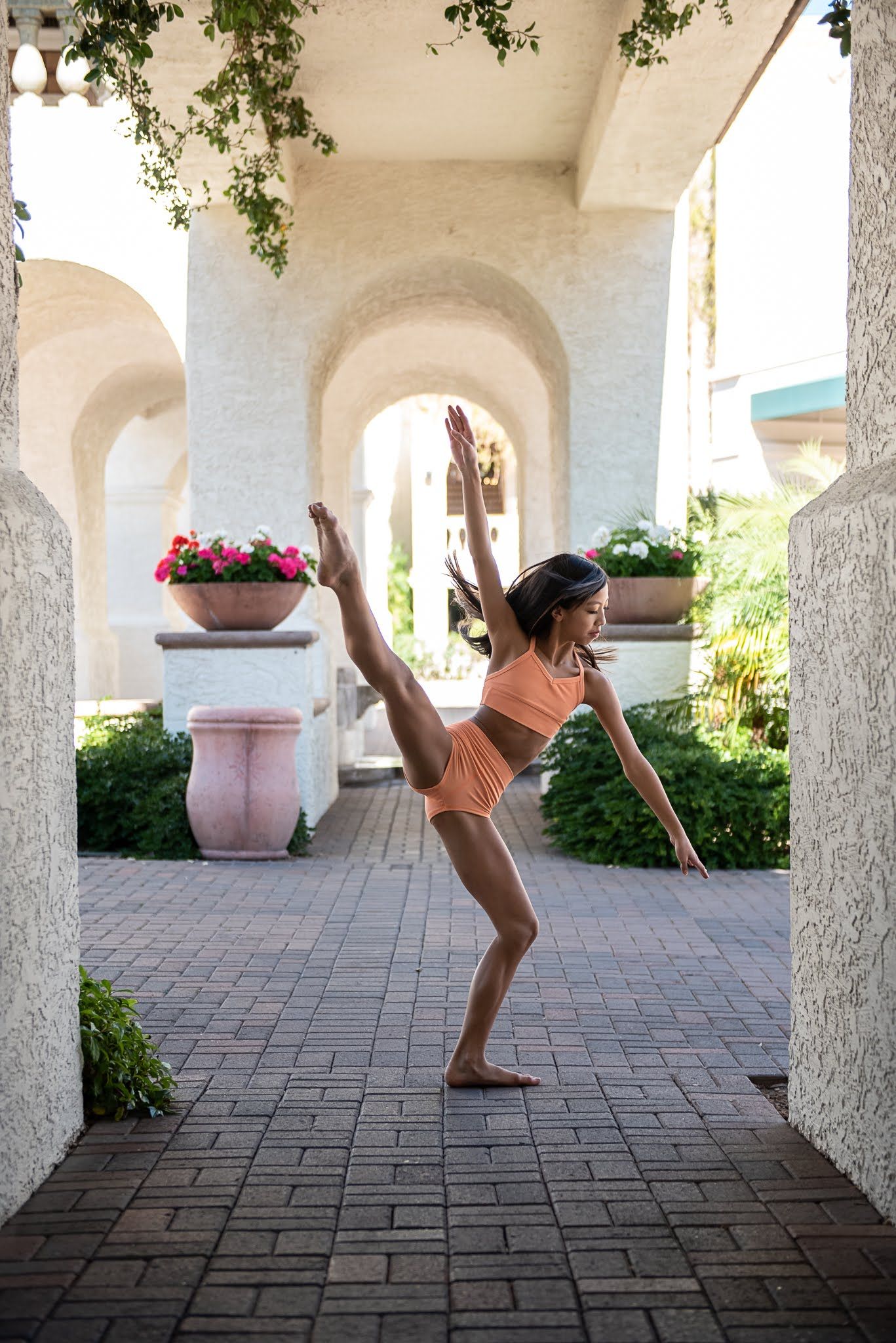 Young female dancer performs a high leg extension in an outdoor archway setting.