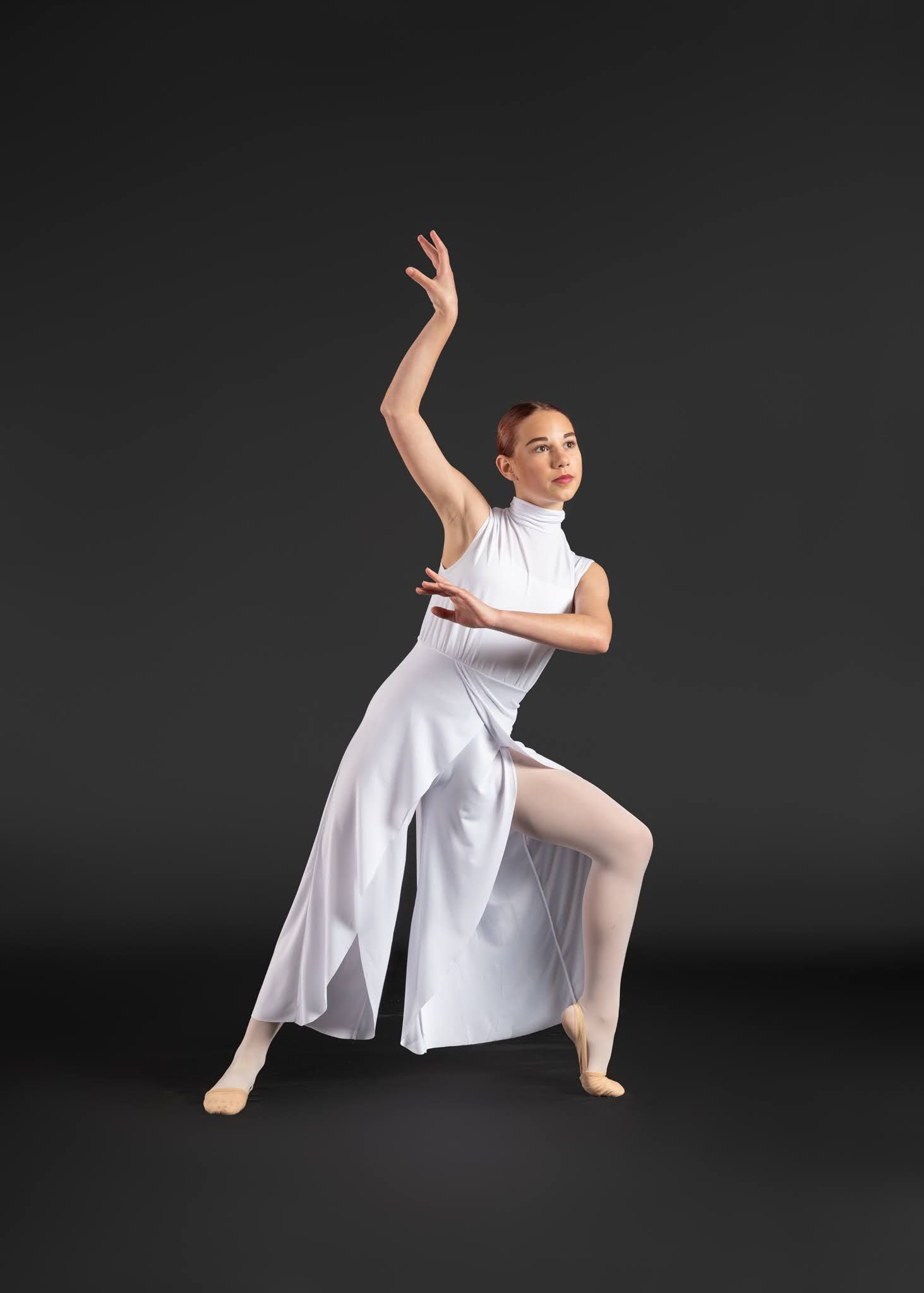 Elegant female dancer in white dress performs a graceful contemporary ballet pose on a dark background.