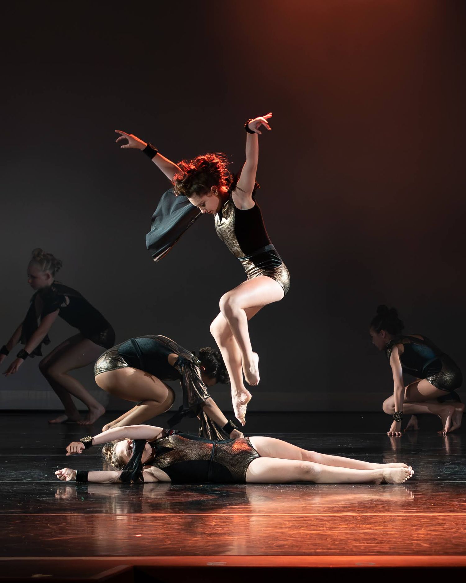 A red-haired dancer leaps above a performer lying on the floor during a contemporary dance performance.
