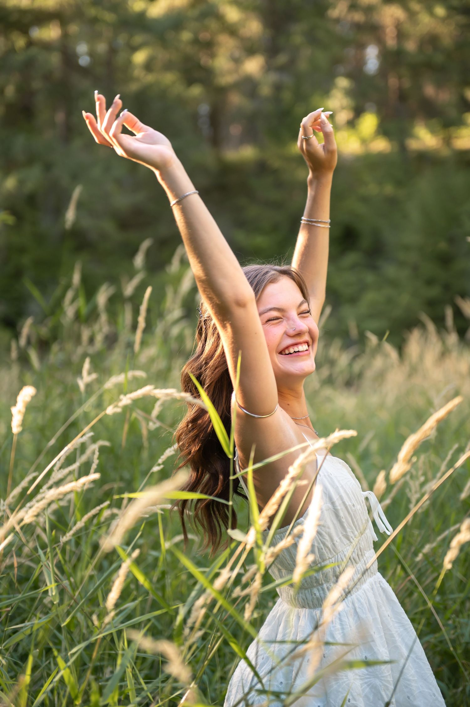 Joyful young woman raises arms in tall grass field at golden hour.