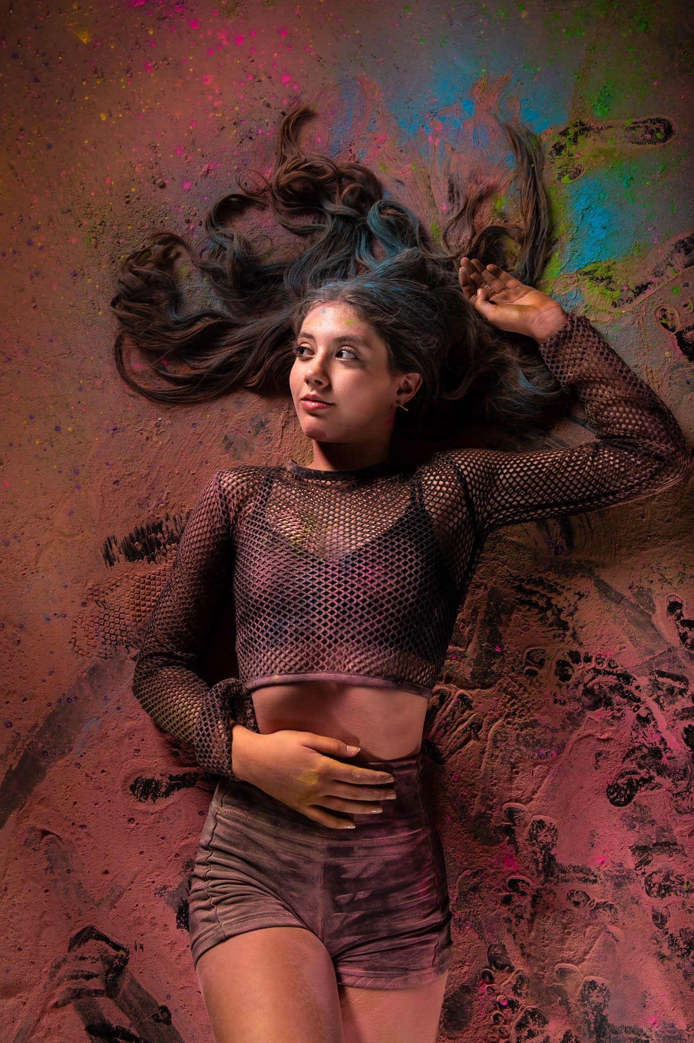 Young female dancer lying on colorful powder-covered ground with hair spread around her head.