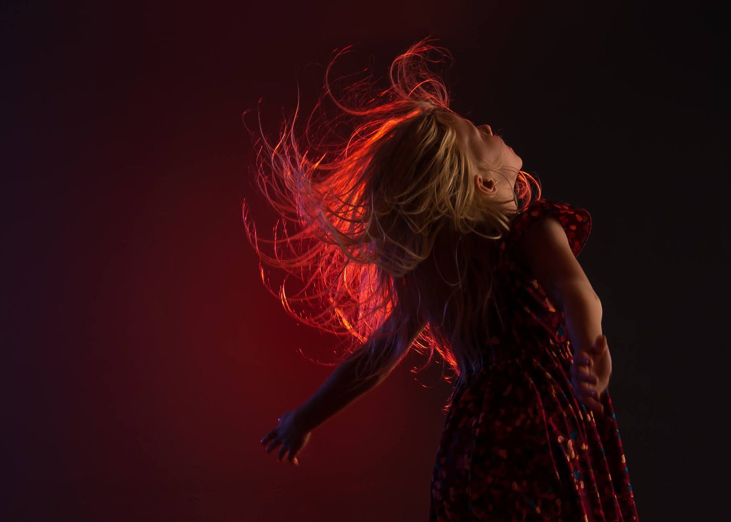 Dancer with hair flying dramatically under vivid red lighting against a dark background in motion.