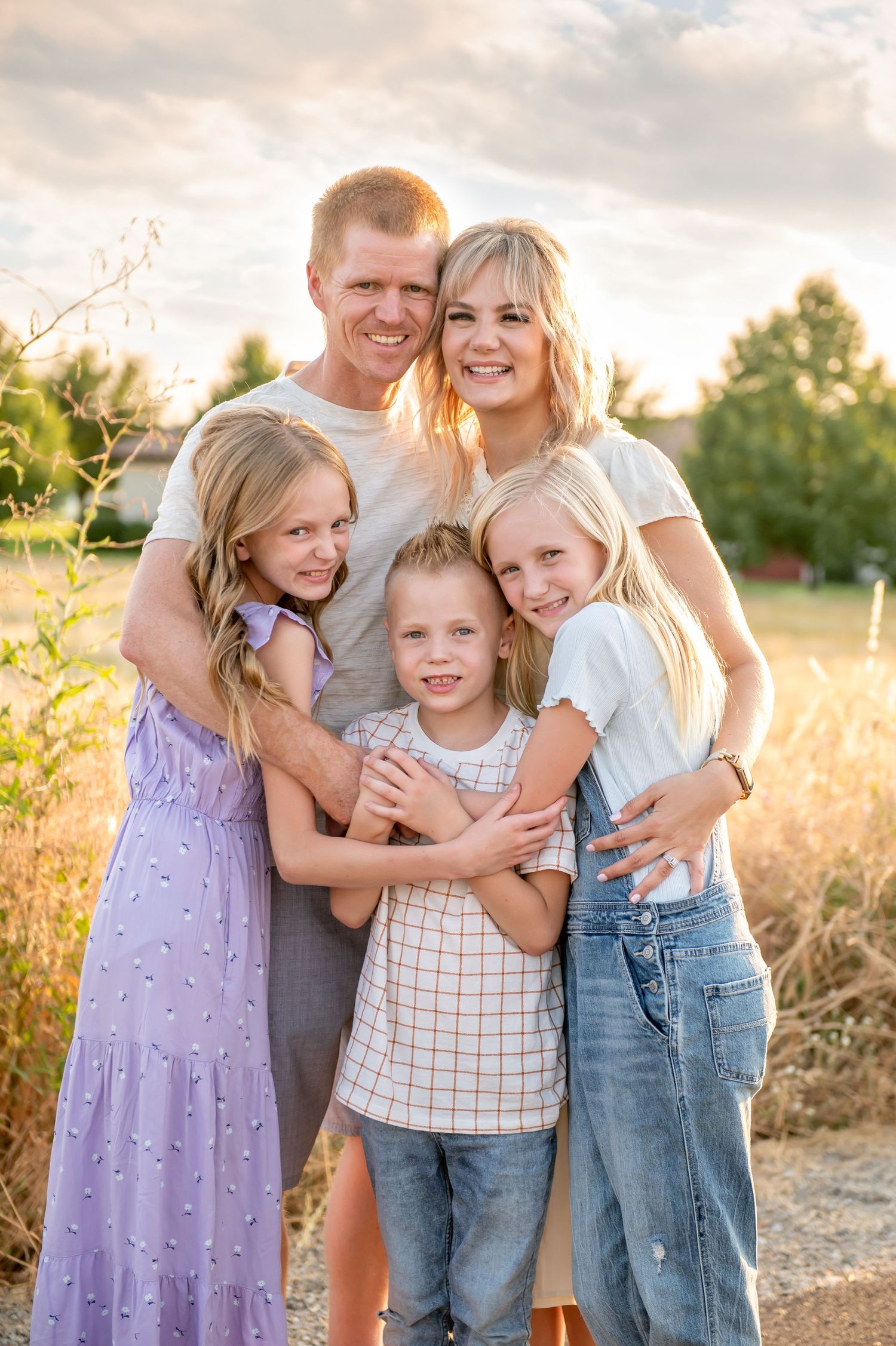 Family of five smiling together in a golden sunset field outdoors.
