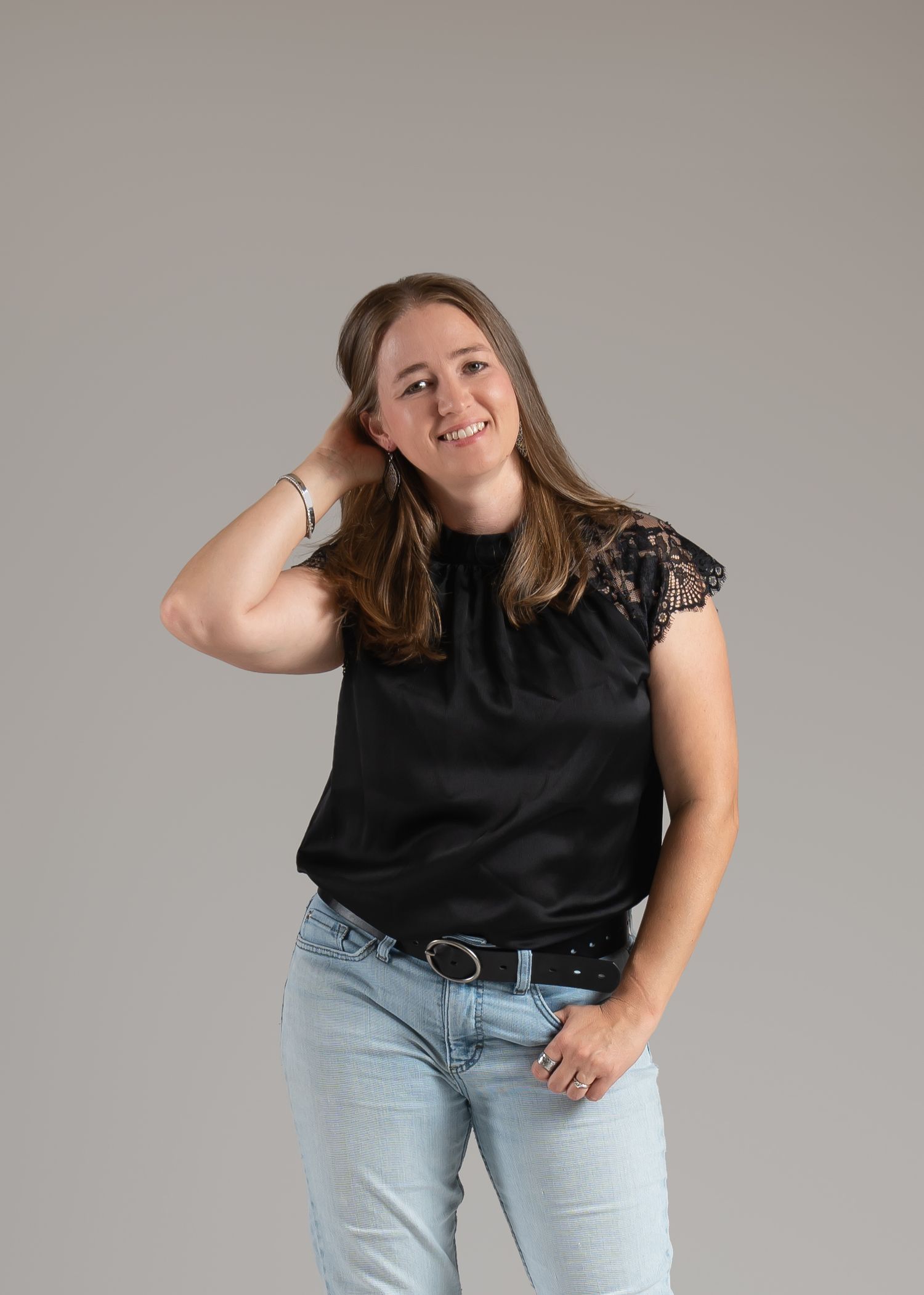 Charlotte Gardunia in a black lace-shoulder top and jeans posing against a neutral gray background.