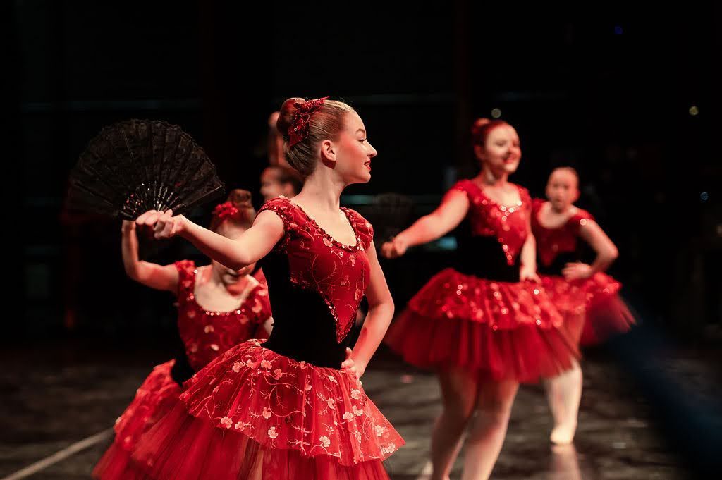 Ballet dancers in red Spanish-style tutus performing with fans during a dance recital.
