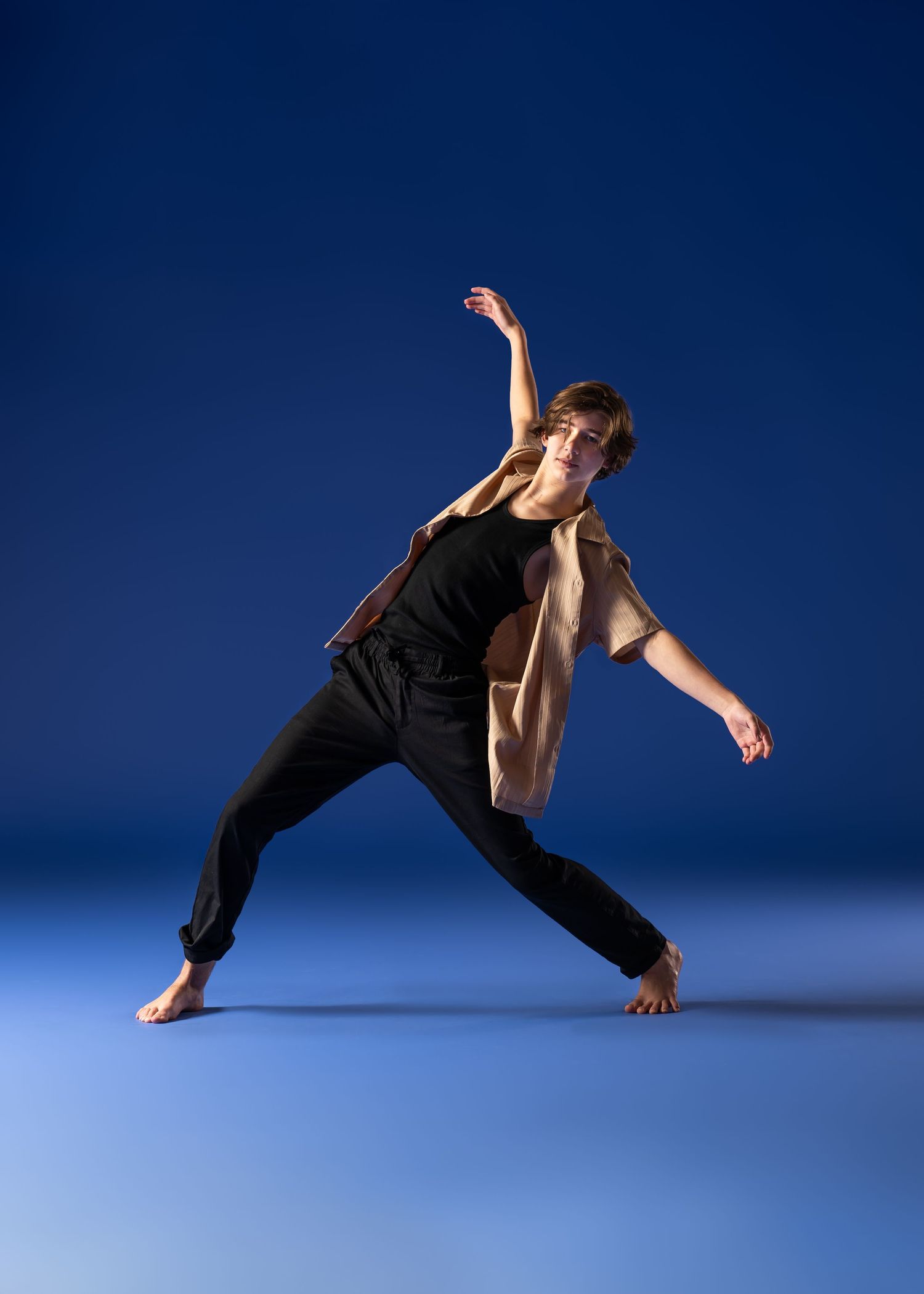 Male contemporary dancer performs expressive pose against blue studio background barefoot.