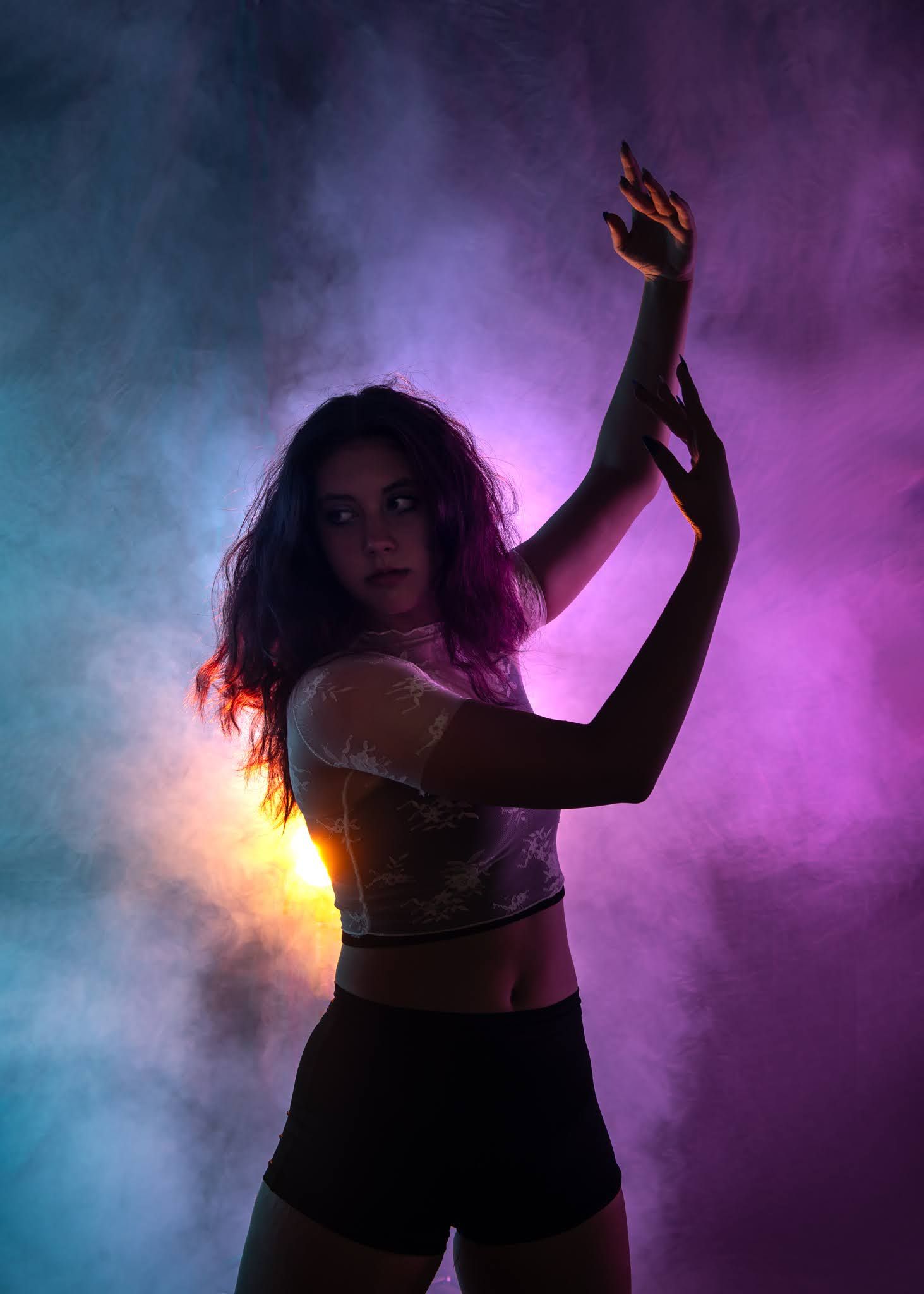 Female dancer posing dramatically in colorful neon smoke purple blue light.
