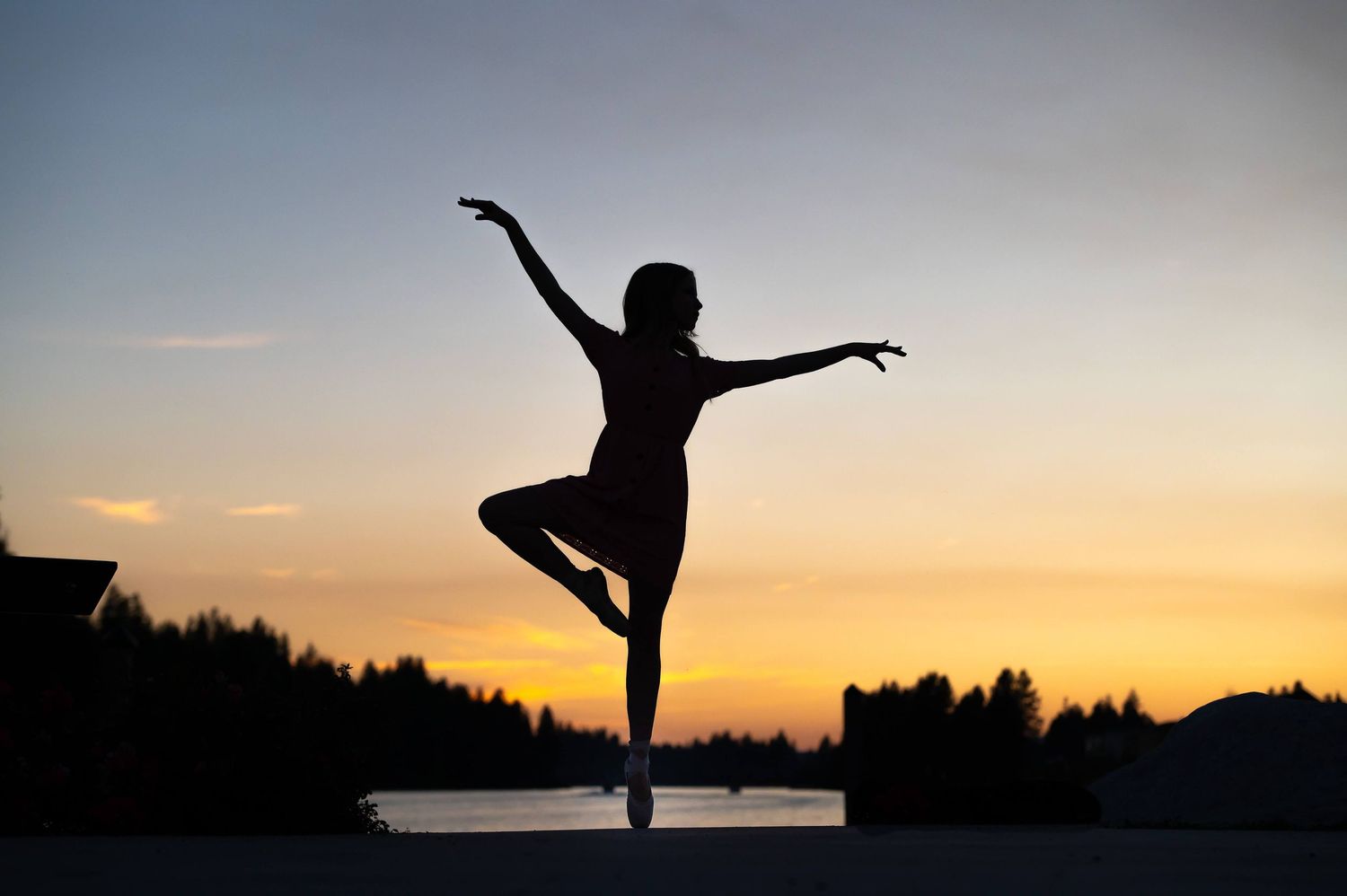 Silhouette of ballerina dancing en pointe against vibrant sunset sky with trees in background.