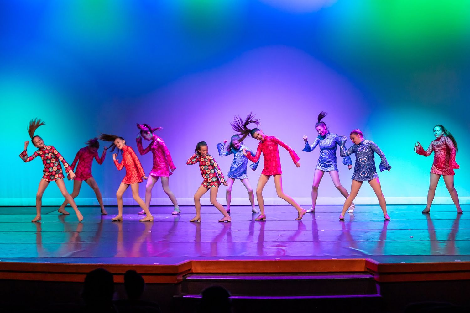 Group of young dancers in colorful costumes perform dynamic routine under vibrant stage lighting.