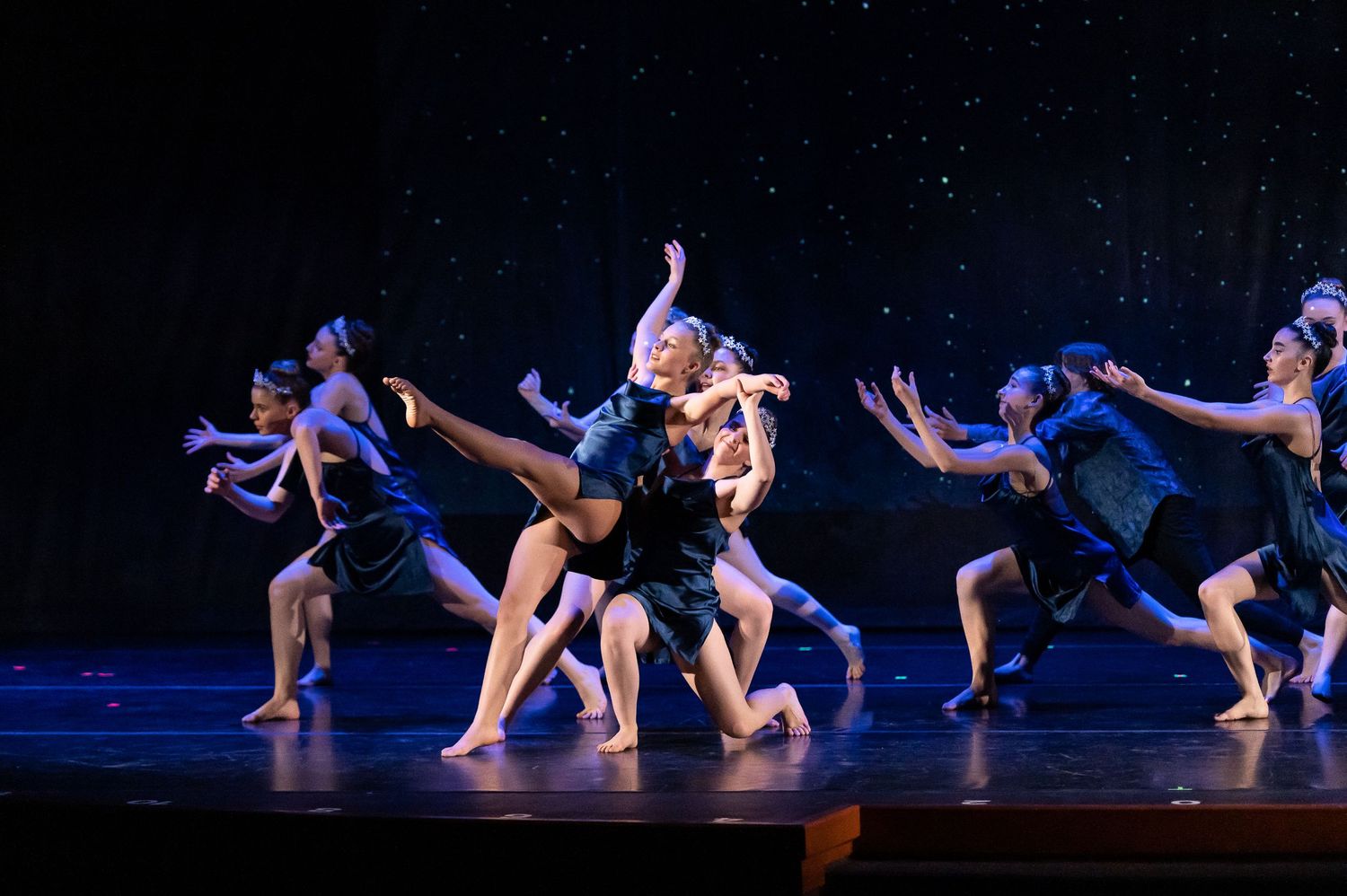Contemporary dance performers in dark costumes executing dynamic movements on a starlit stage.