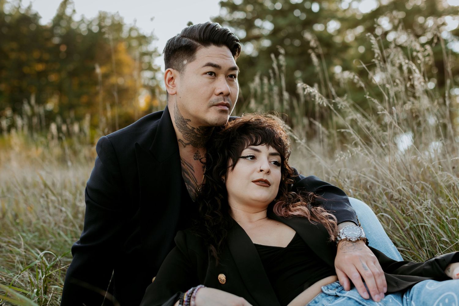 Couple sitting together in tall grass field, woman resting on mans shoulder.