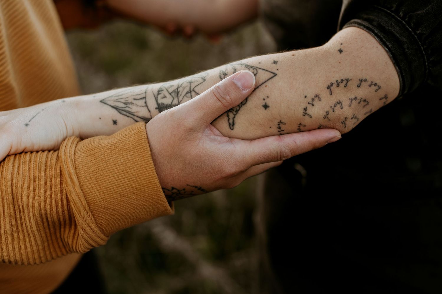 Close-up of two tattooed arms intertwined, showcasing intricate ink designs on pale skin.