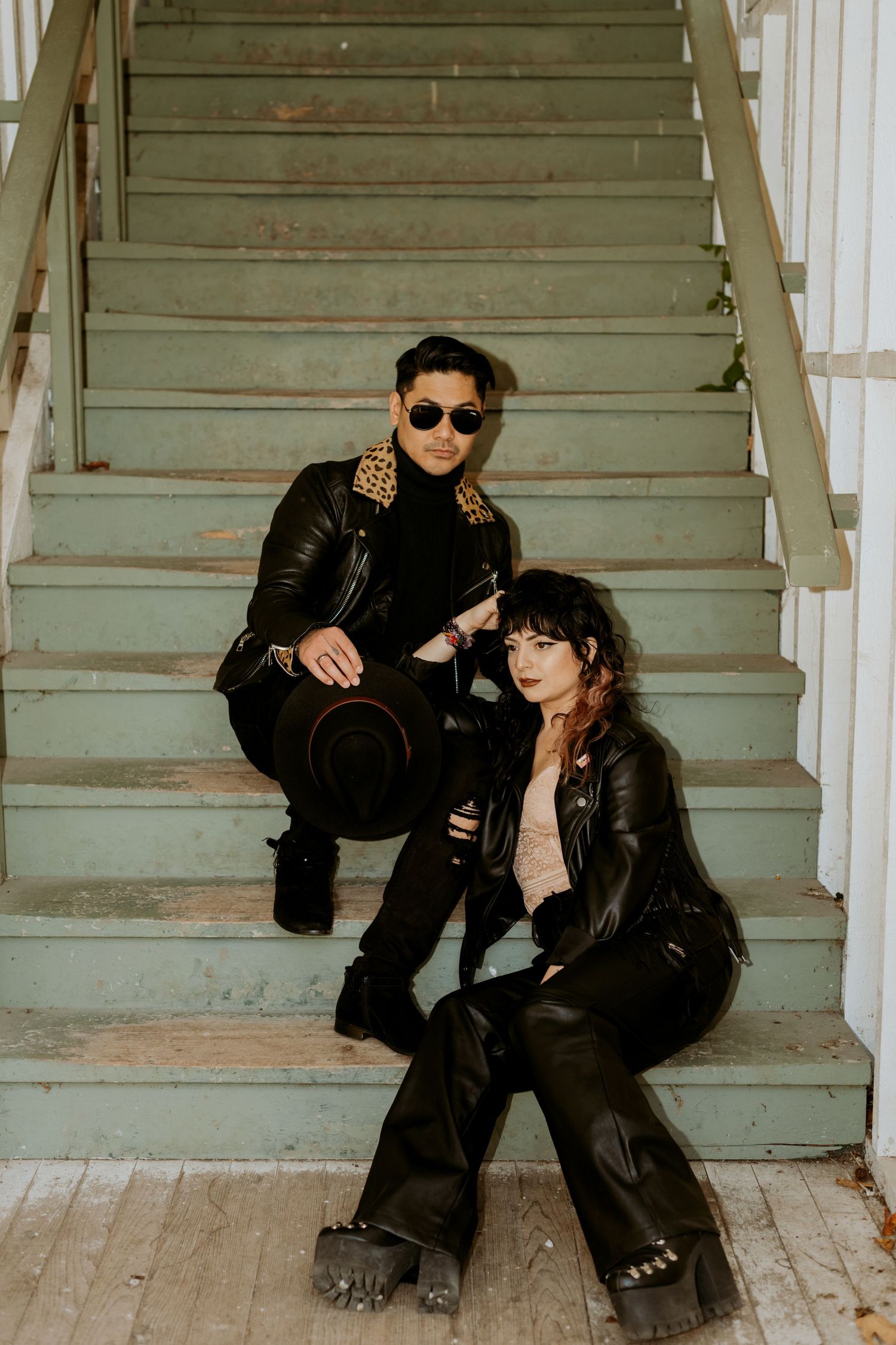 Edgy couple posing on weathered green stairs in coordinating black leather jackets.