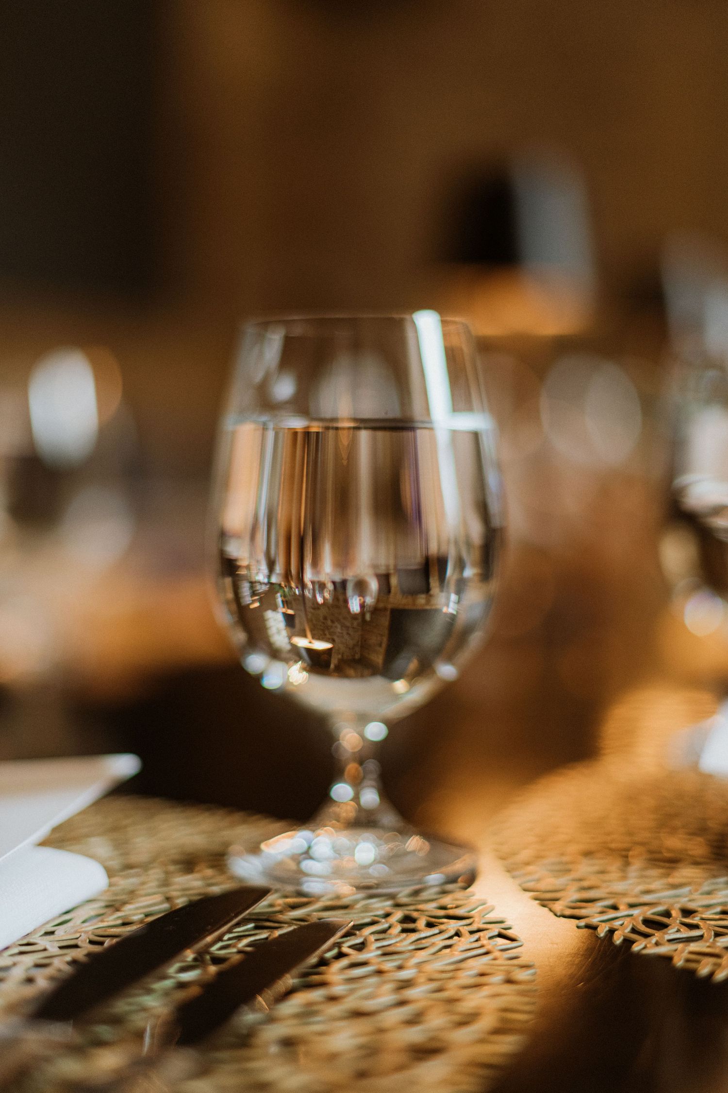 Crystal clear water glass on gold lace charger plate at elegant wedding reception table.