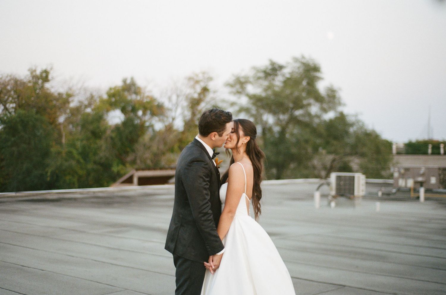 Bride and groom sharing a tender kiss on a rooftop with trees in the background.