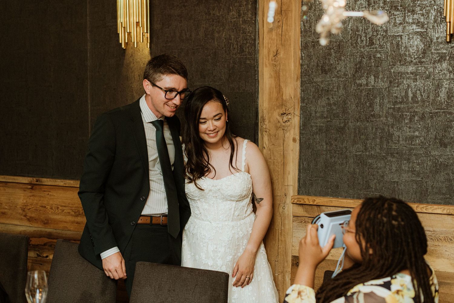 Wedding guest photographs smiling bride and groom at elegant reception venue.