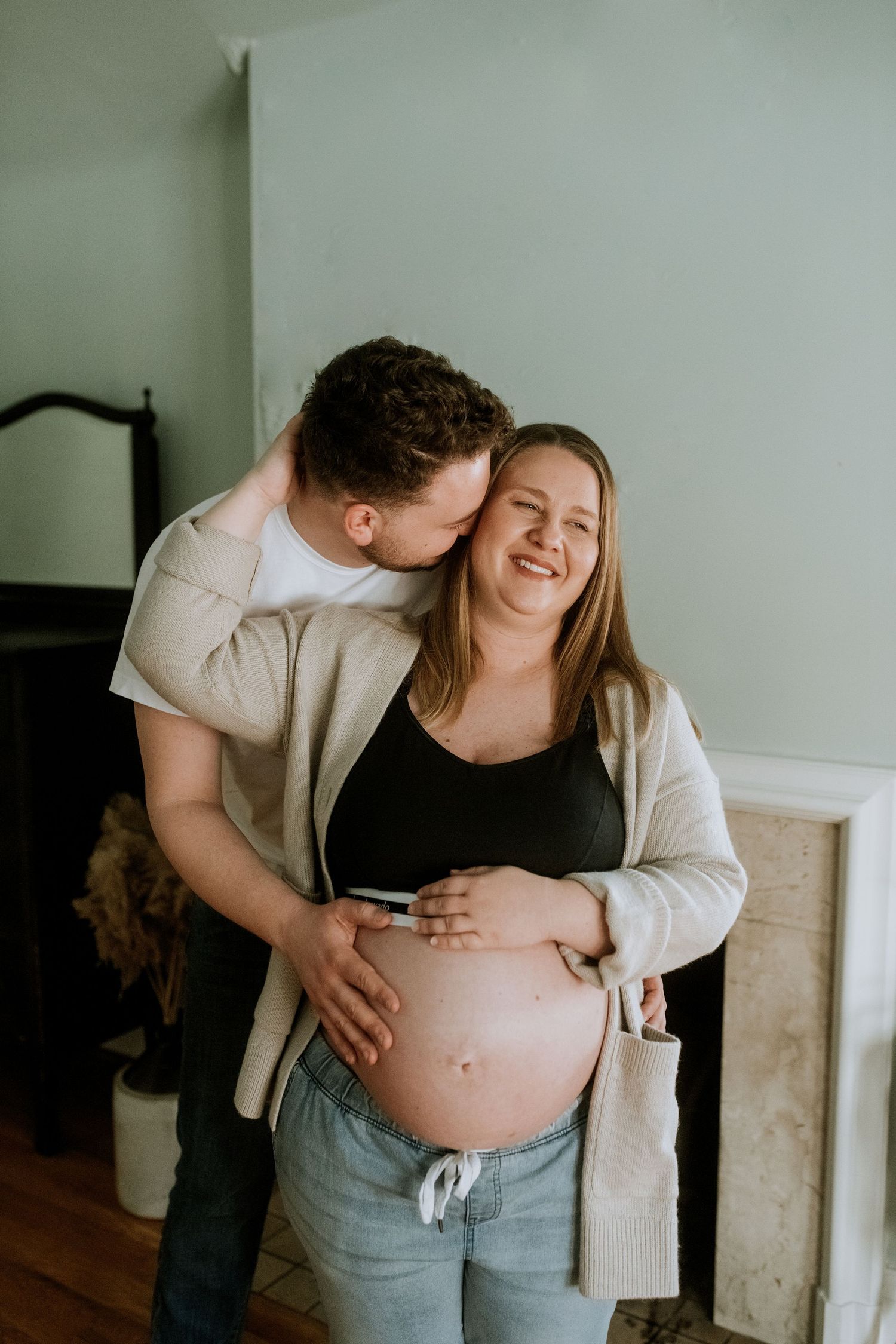Happy couple shares tender moment indoors as man kisses pregnant partners cheek.