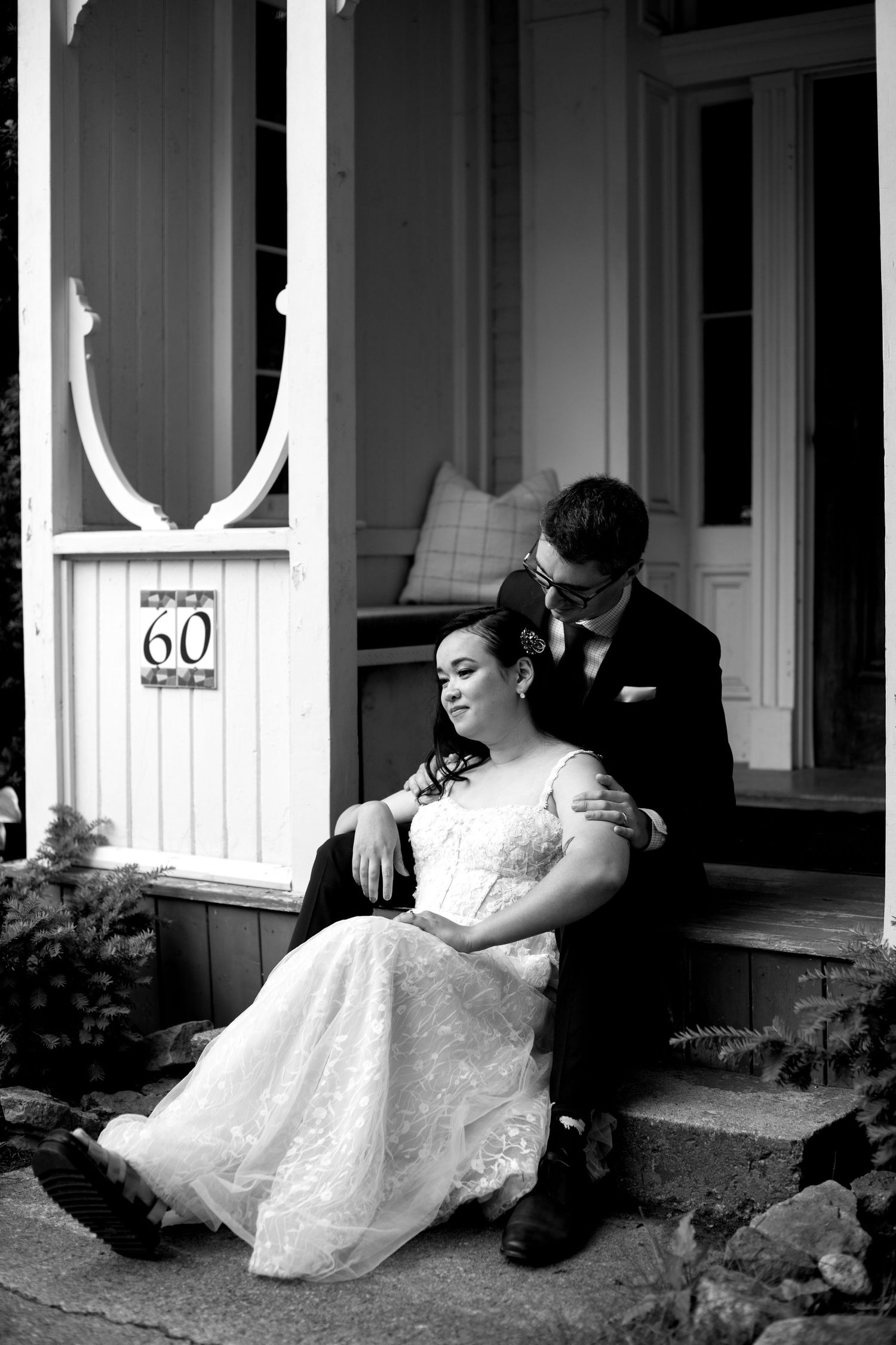 Black and white photo of bride and groom sitting on steps of a historic building numbered 60.