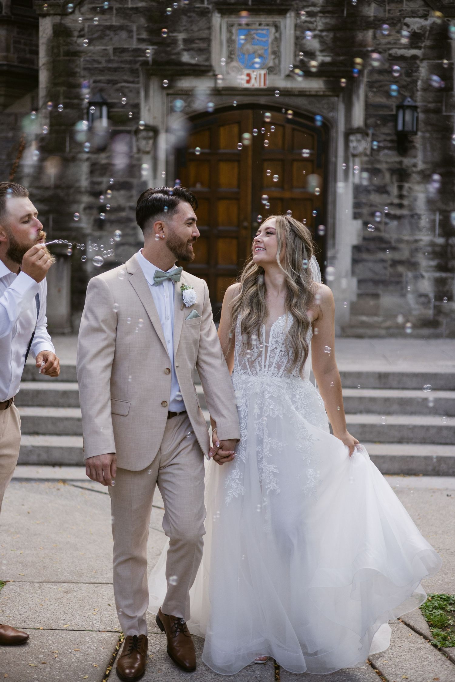 Bride and groom share a loving glance while walking through bubble send-off at stone venue.