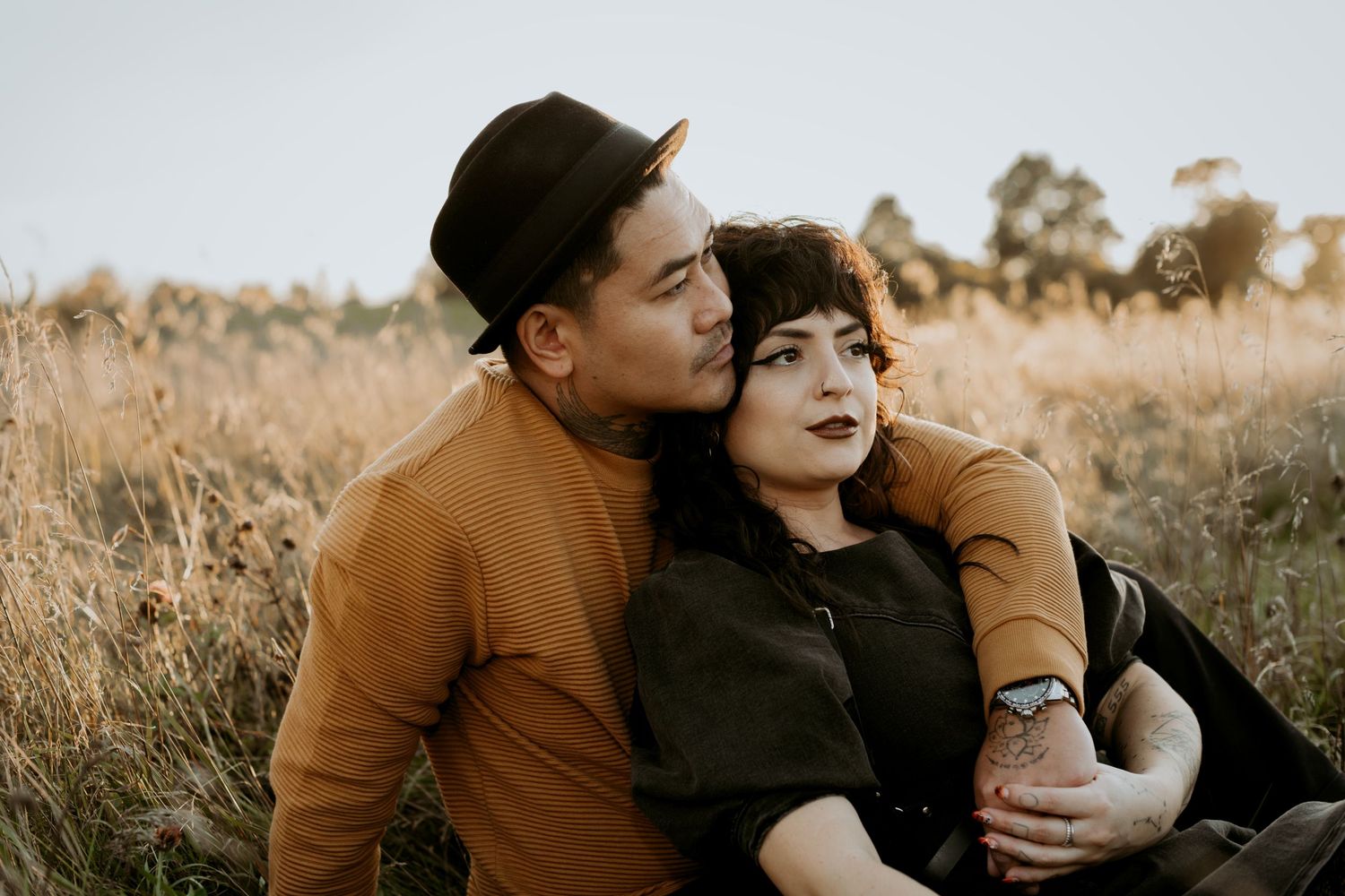 Man in black hat kissing woman's cheek while sitting in a golden grass field.