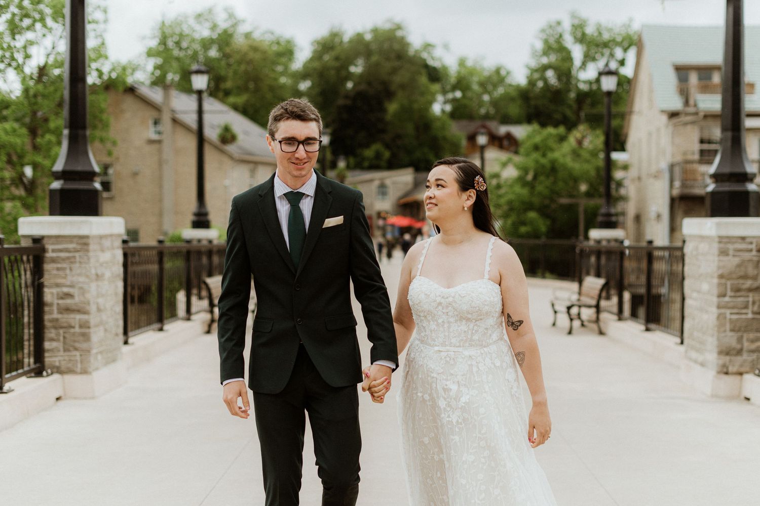 Elegant bride and groom walk hand in hand along a stone pathway in a charming town.